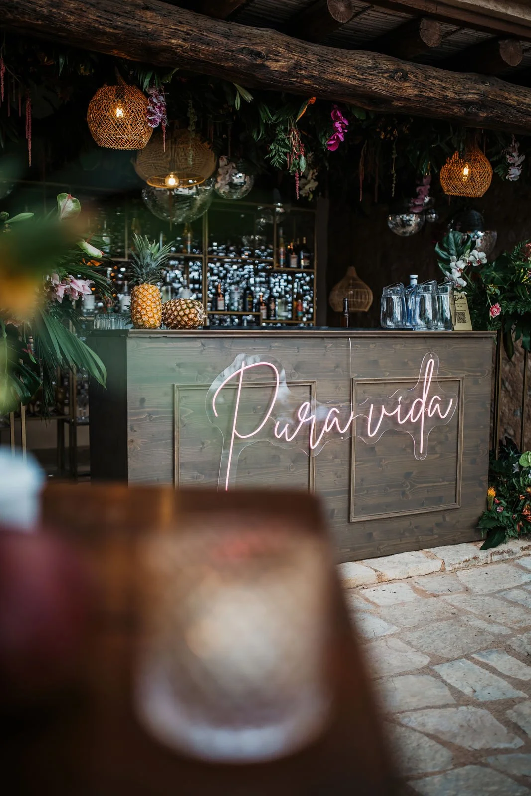 A bar area decorated with tropical plants, pineapples, and a neon sign that reads 'Paravida'.