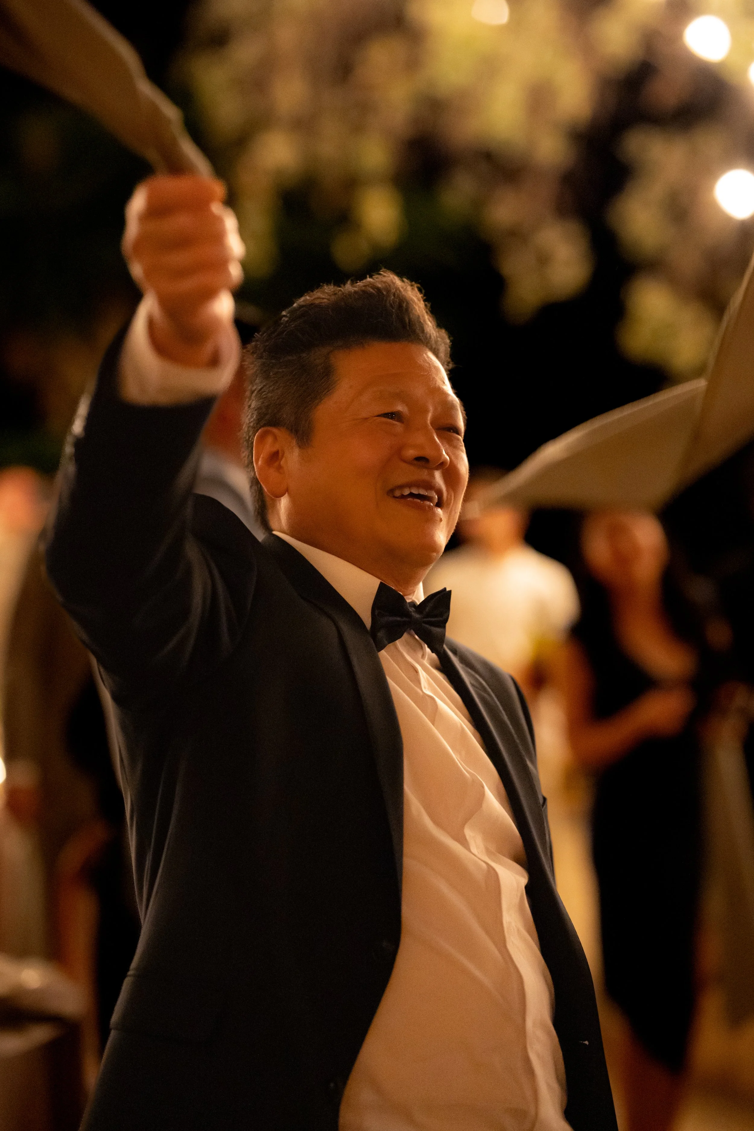 Man in tuxedo raising his hand at a celebration or event during the evening.