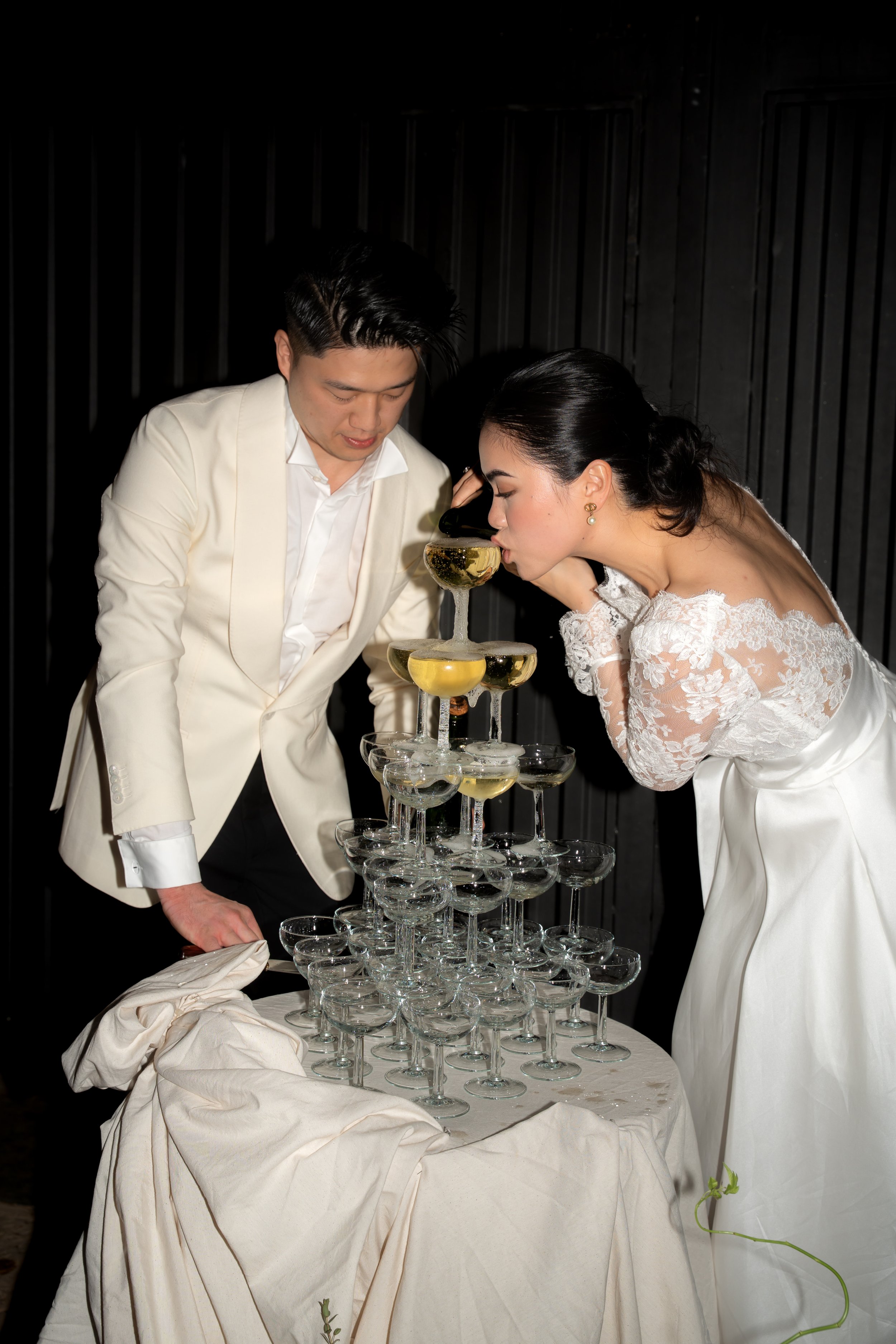Couple in wedding attire pouring champagne into a champagne tower.