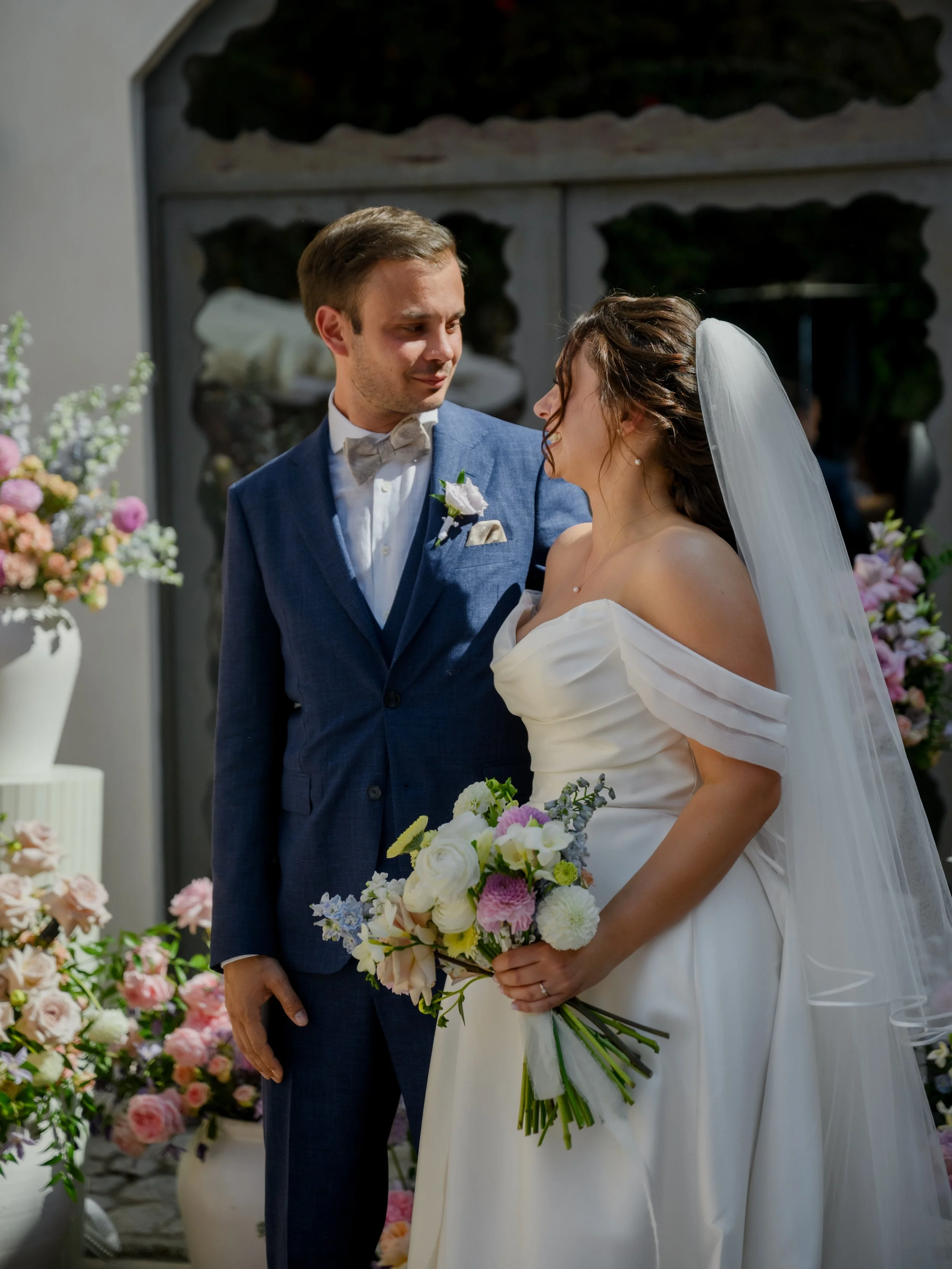 A bride and groom sharing a moment during their wedding ceremony with floral arrangements in the background.