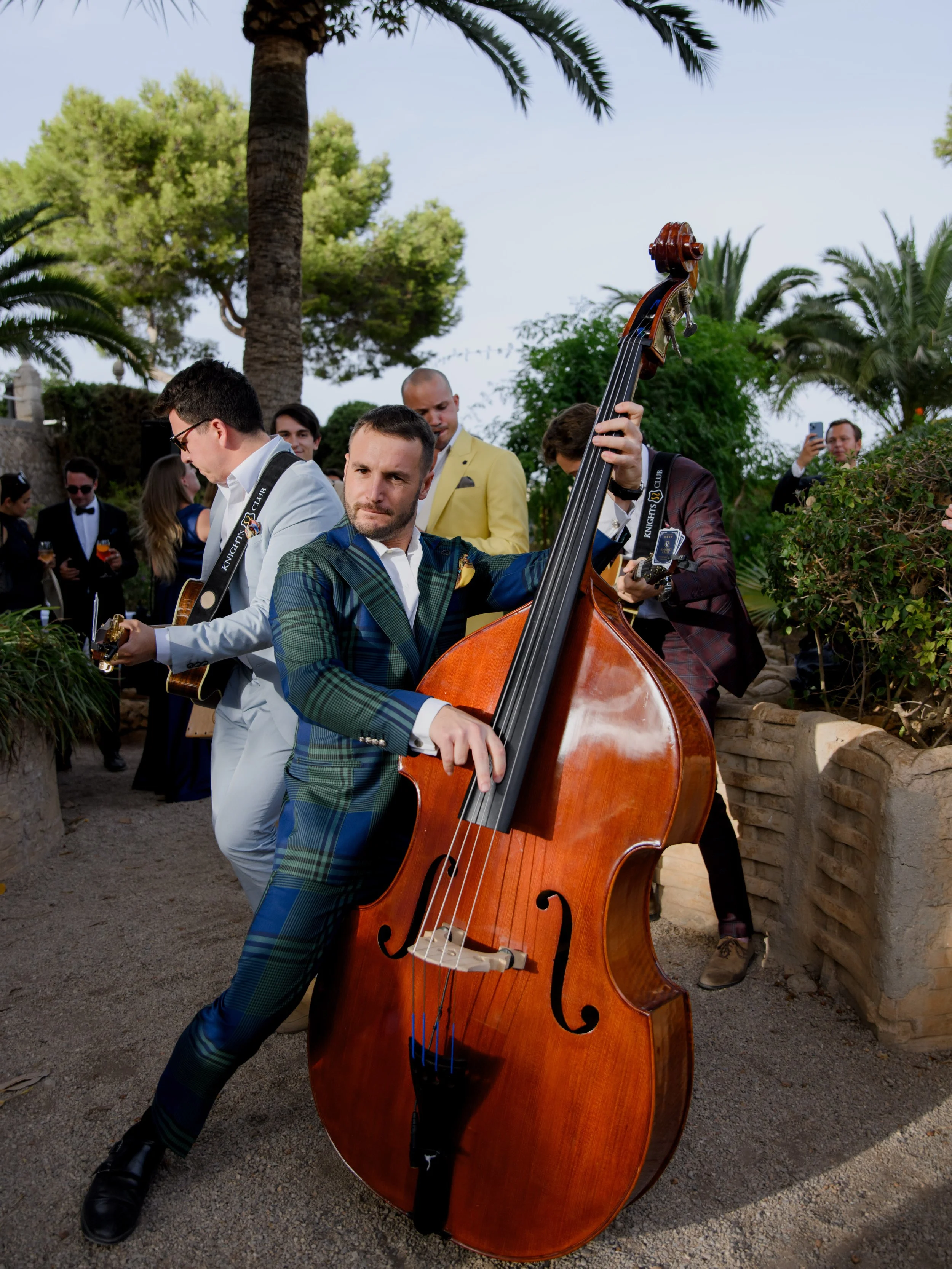 Man playing double bass at outdoor event with guests in formal attire