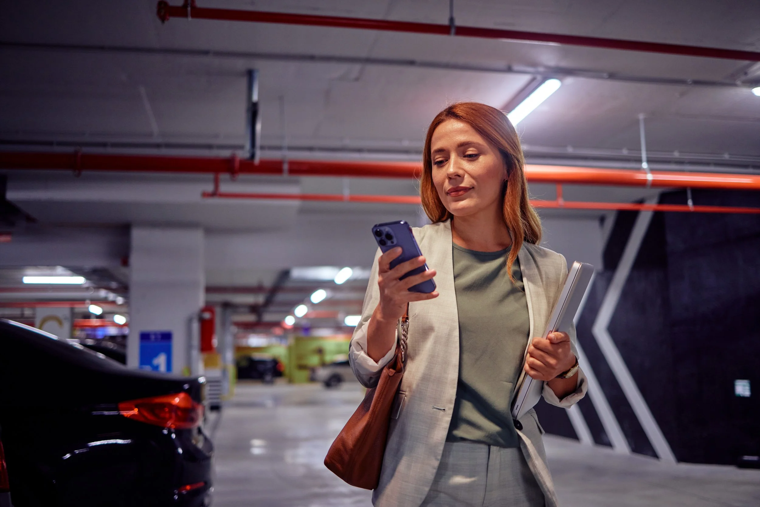 A woman standing in a parking garage, using her phone to purchase parking.