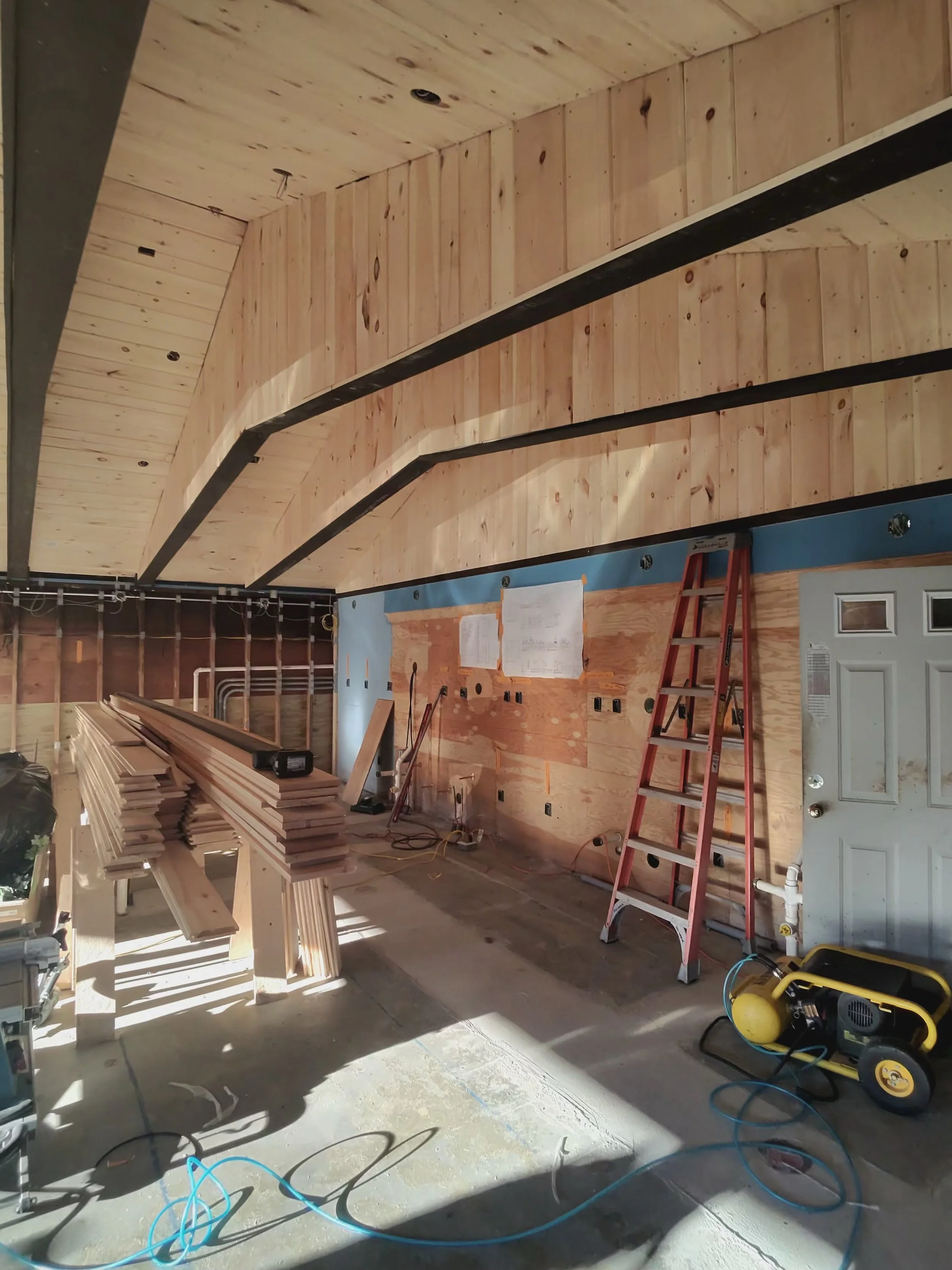 Interior of a building under construction with wooden wall paneling and a red ladder, construction tools, and materials on the floor.