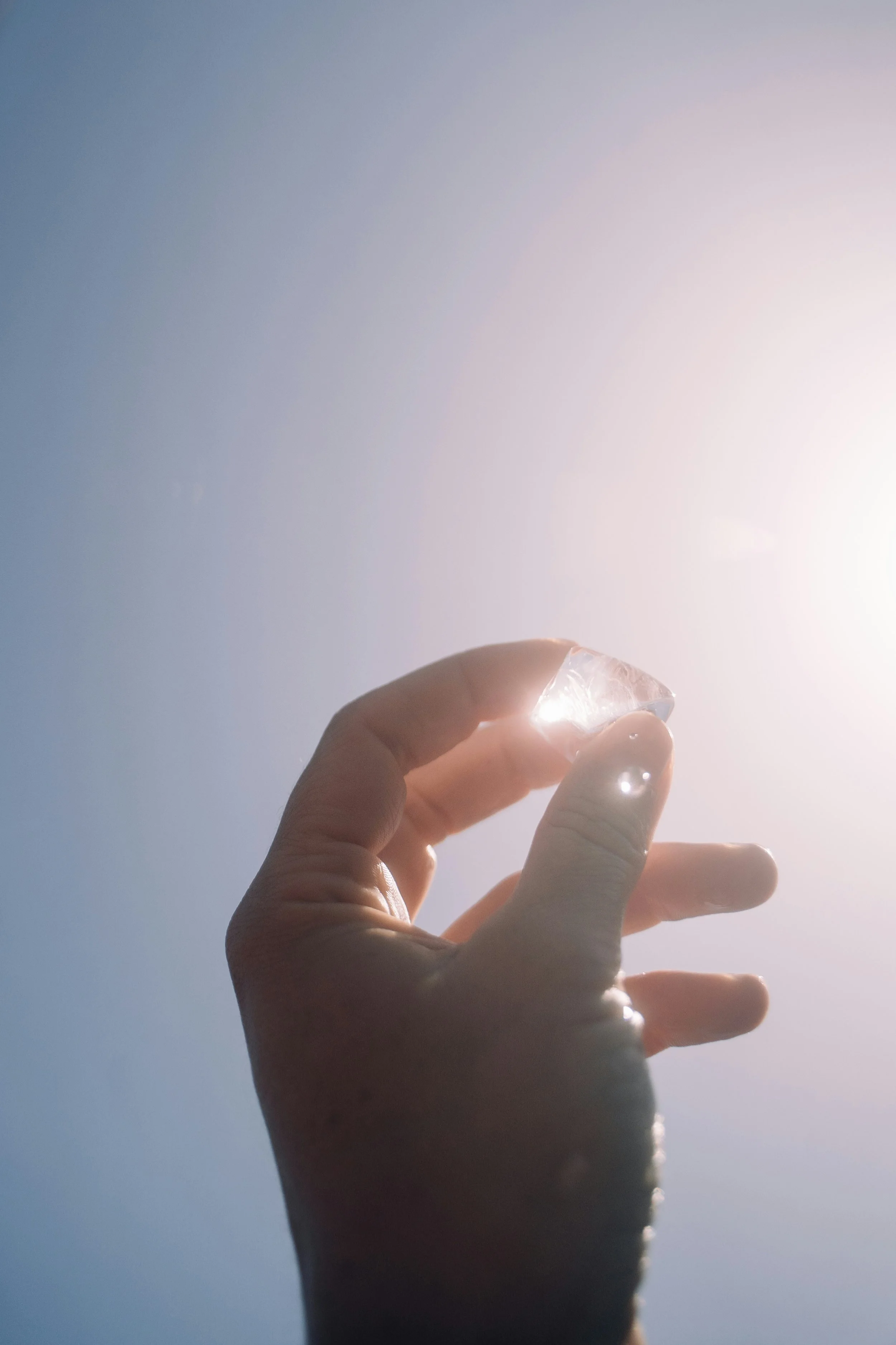 Hand, die einen klaren Kristall vor hellem Sonnenlicht hält.