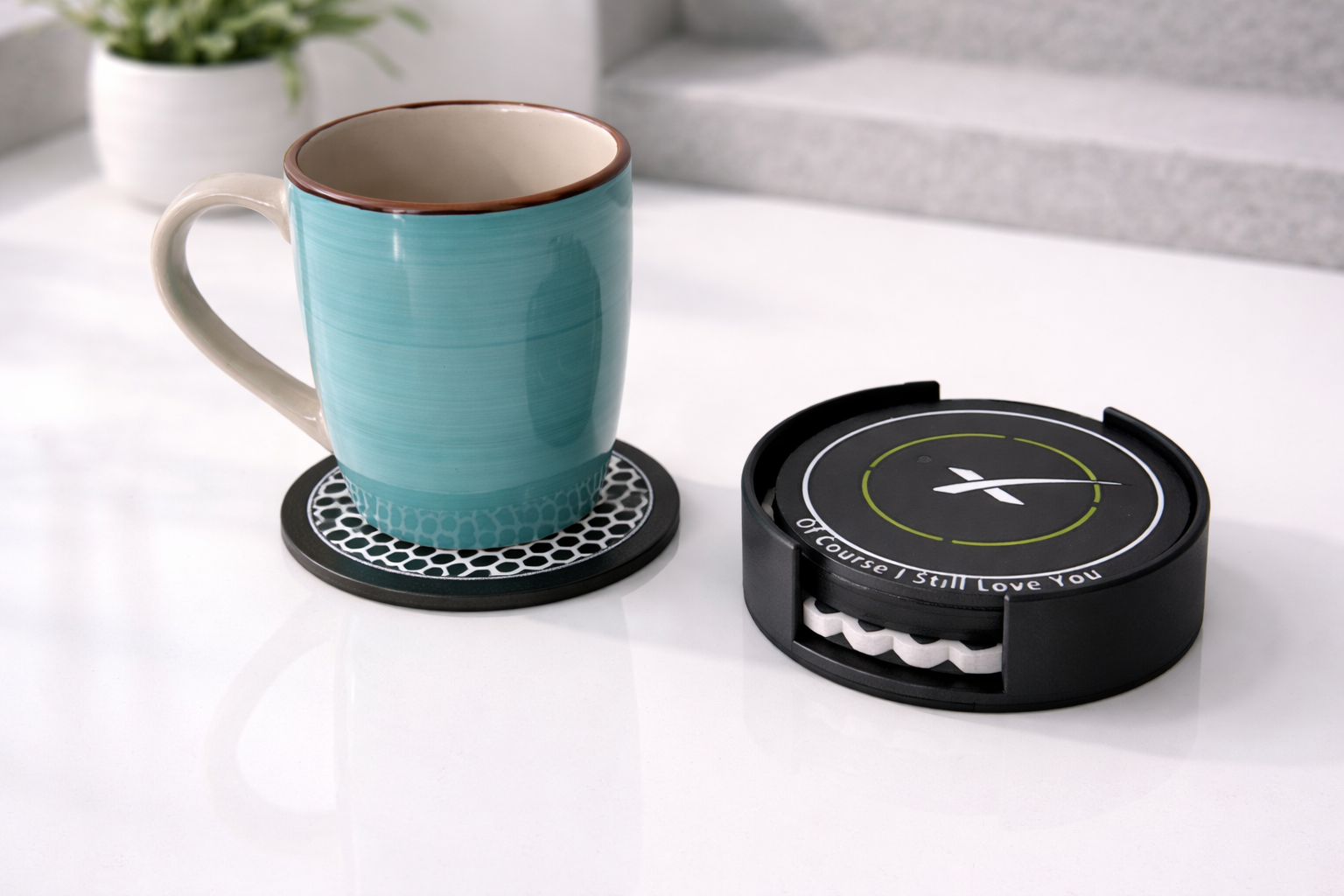 A blue ceramic mug with a brown rim on a black and white coaster, next to a spacex coaster set, on a white countertop.