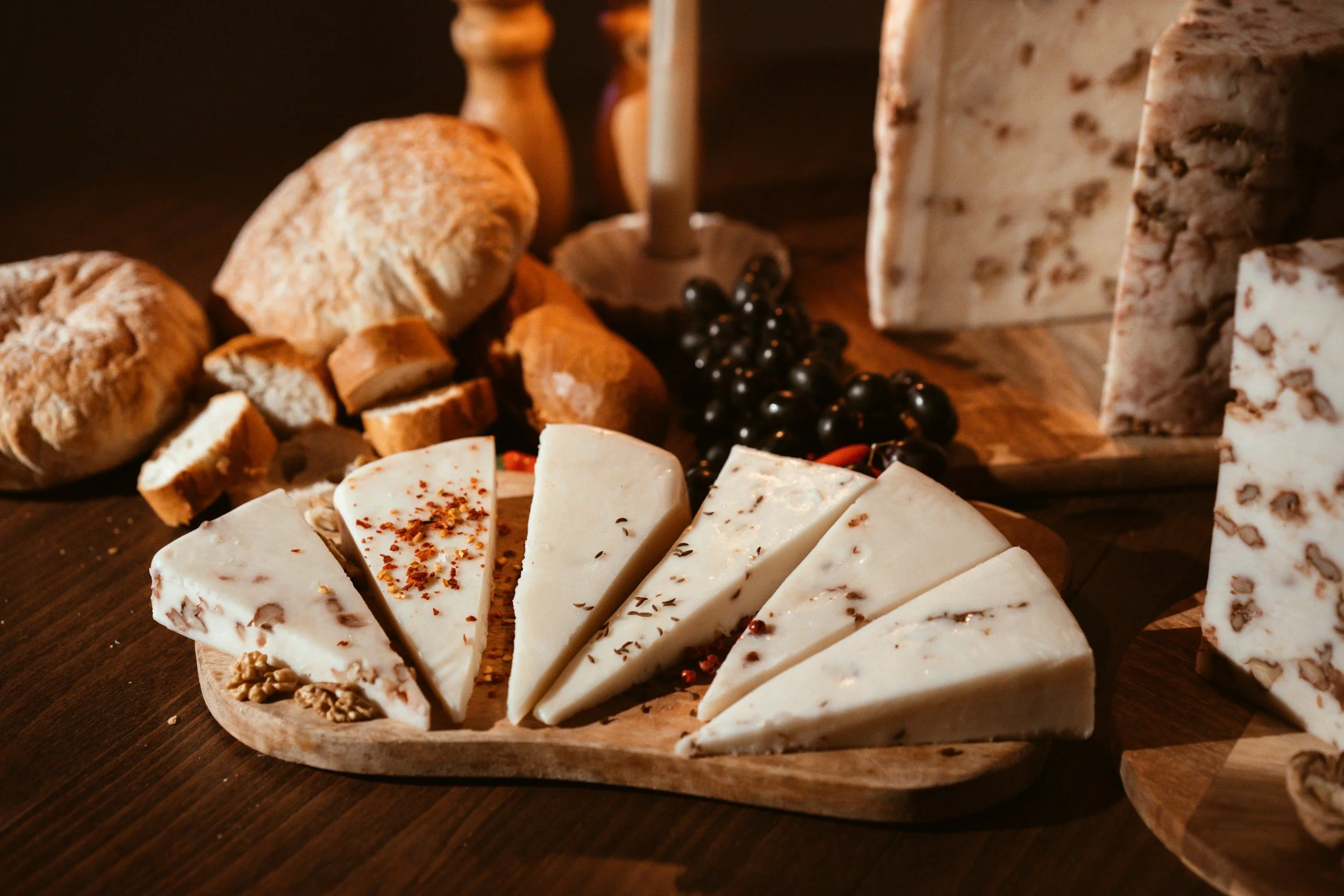 Assorted cheeses, bread rolls, and black grapes on a wooden table from The Charcuterie Chics near Boone NC