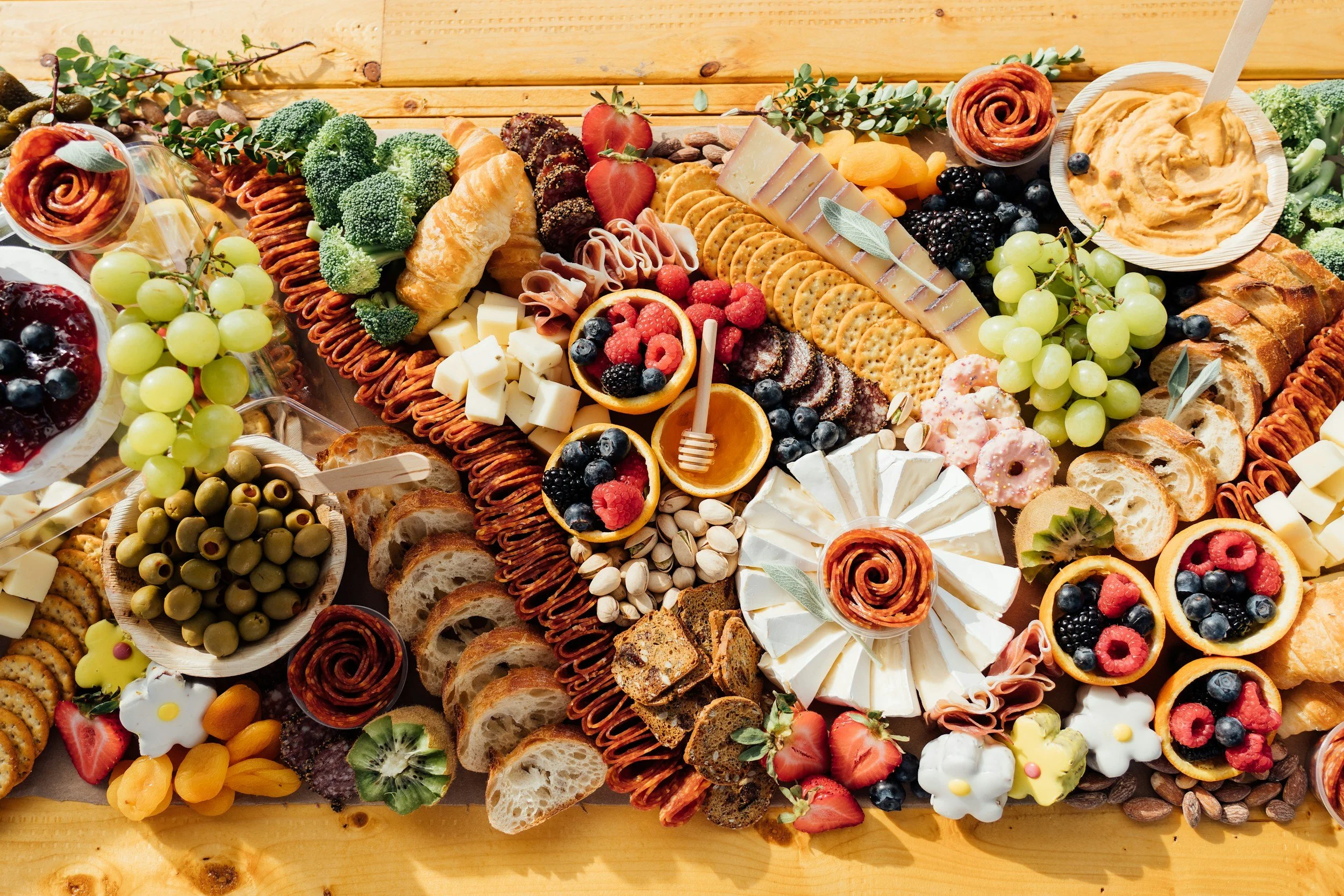 Assorted cheeses, fruits, crackers, bread, and dips on a wooden table from The Charcuterie Chics near Cary NC for an anniversary party
