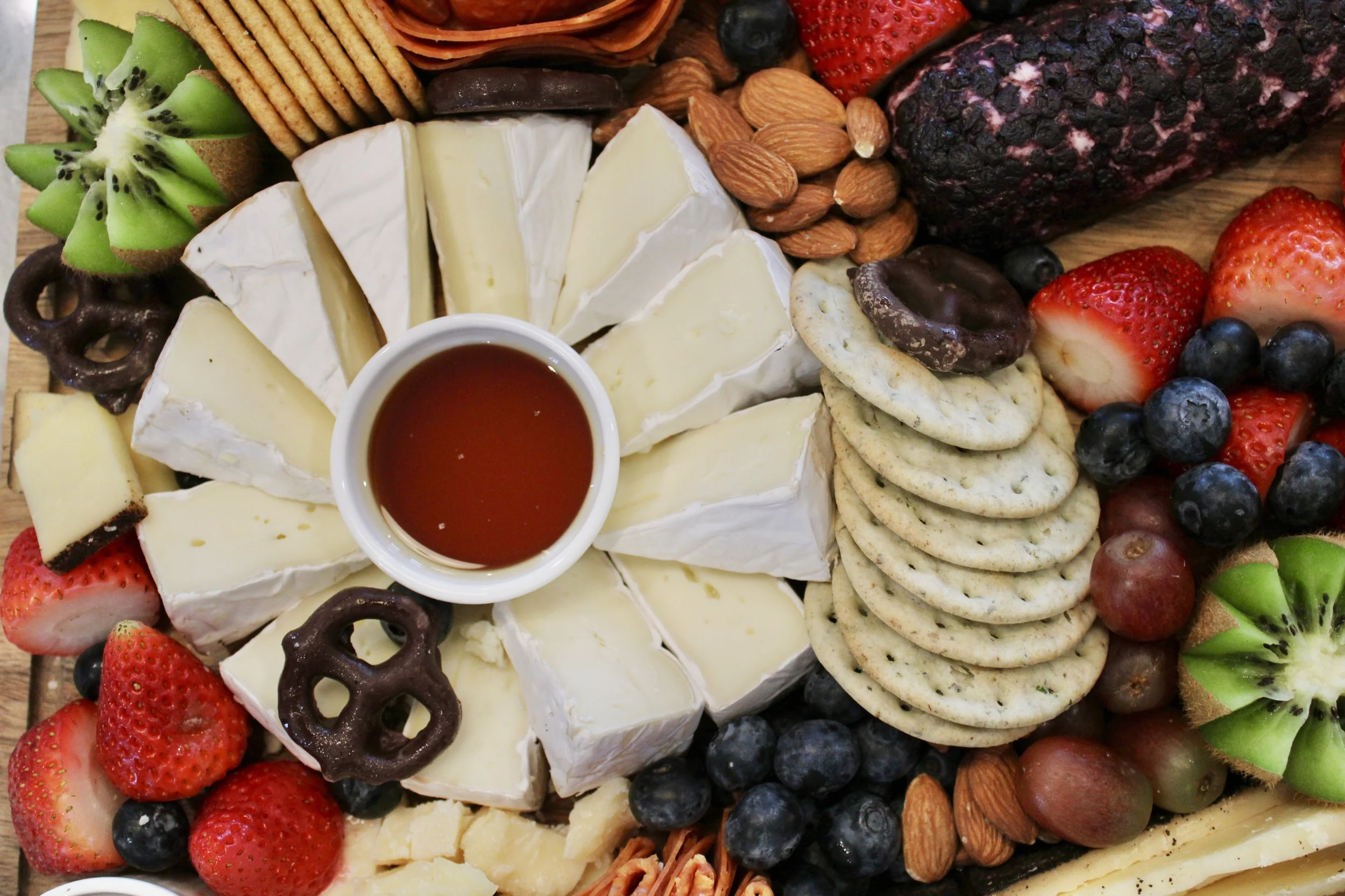 A cheese platter with assorted fruits, crackers, nuts, and a small bowl of honey or syrup at the center from The Charcuterie Chics near Chapel Hill NC for a birthday party