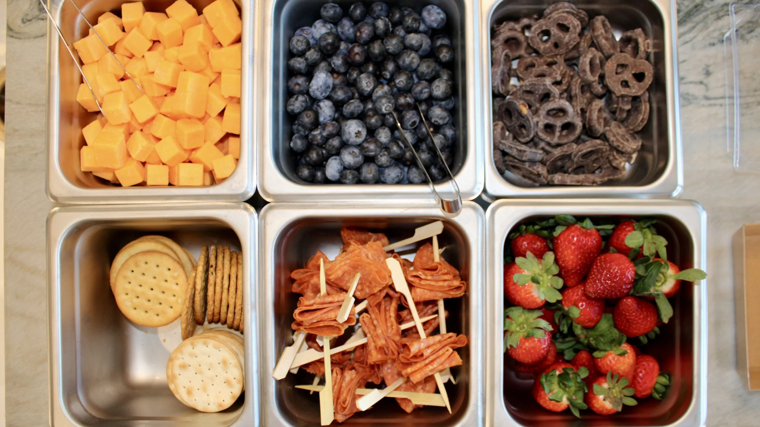 Mobile charcuterie cart with blueberries, chocolate-covered pretzels, crackers, pepperoni slices with toothpicks, and fresh strawberries with green leaves from The Charcuterie Chics near Raleigh NC