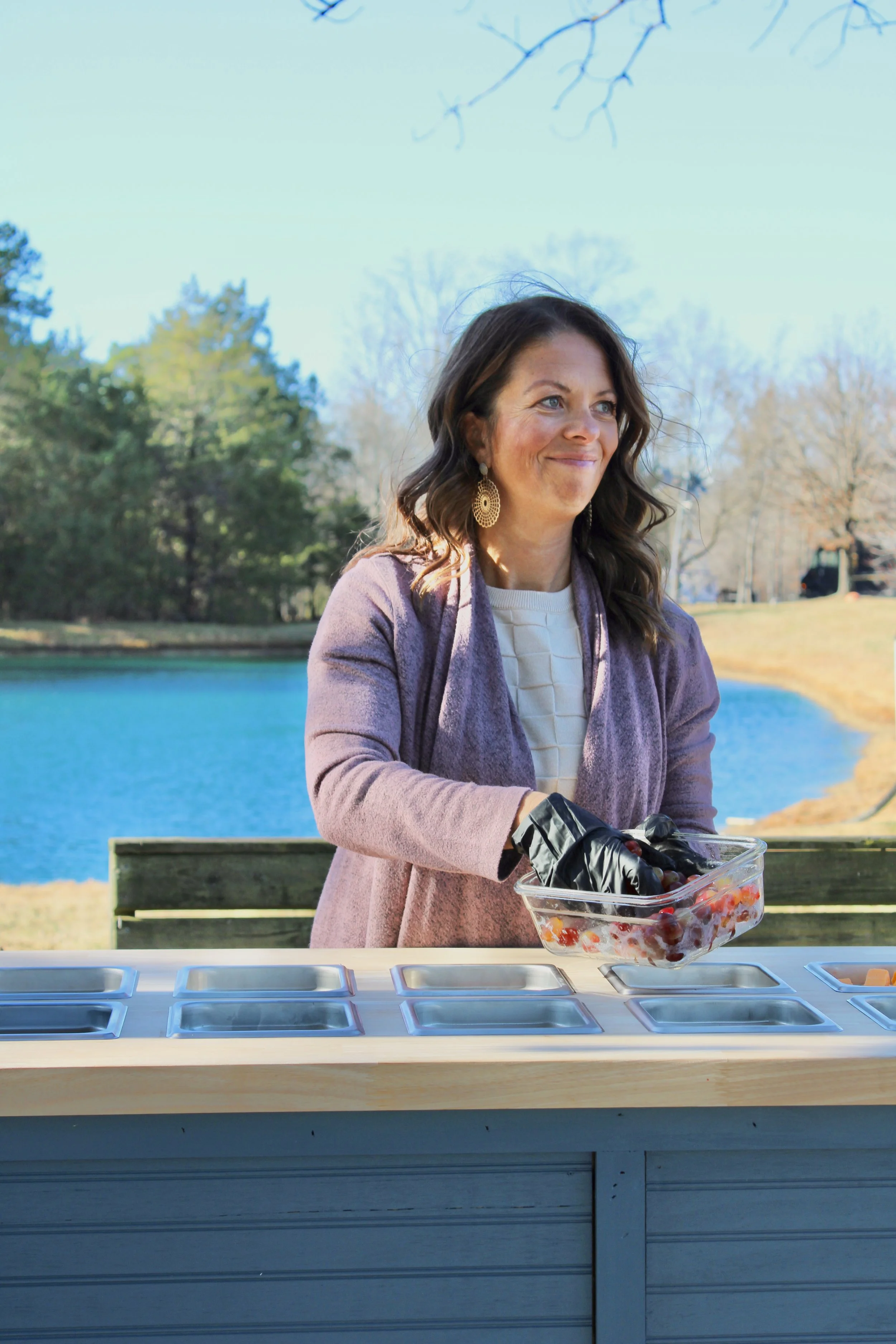 Amber in a purple coat preparing strawberries in a clear plastic container for her mobile charcuterie cart for an event near Concord NC