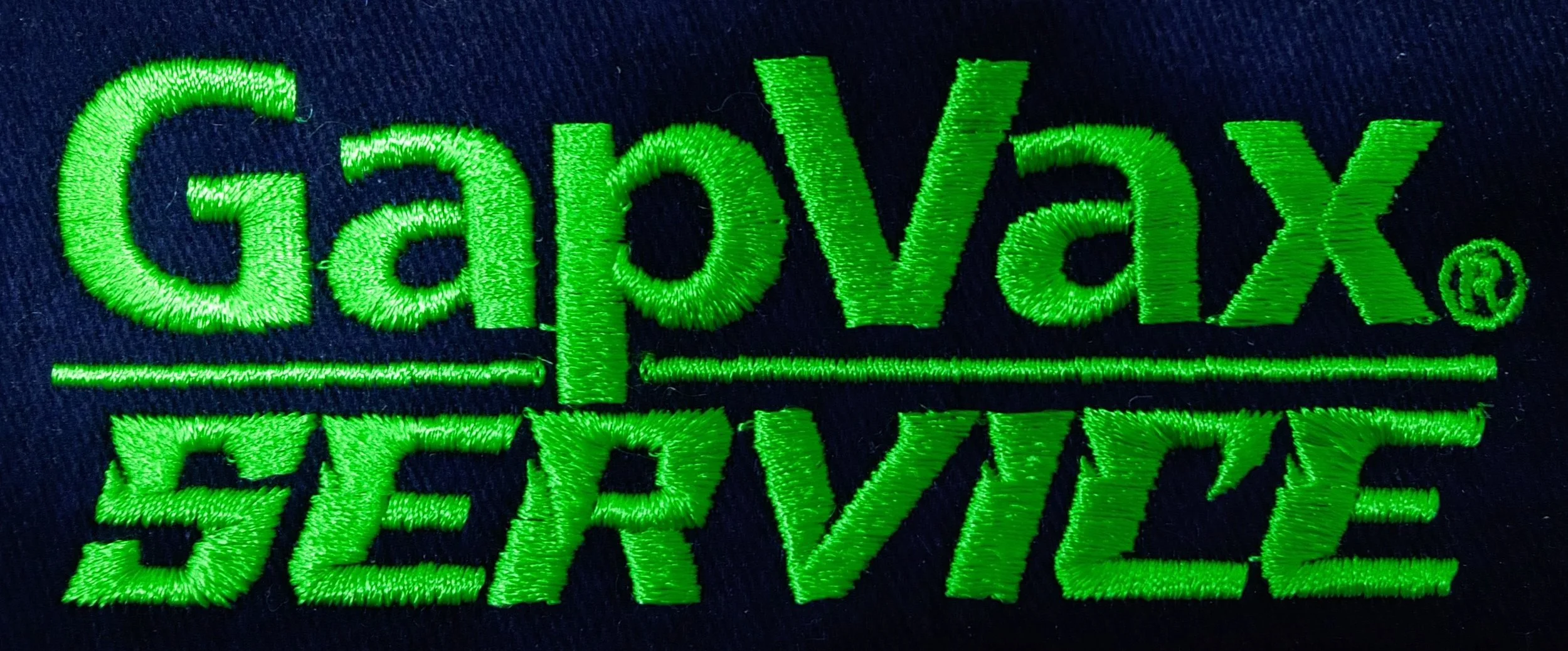 Close-up of green embroidered patch with the words "GapVax SERVICE" on dark fabric background.