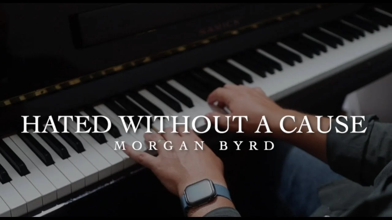 Close-up of a person's hands playing a piano with the song title 'Hated Without a Cause' and 'Morgan Byrd' written on it.
