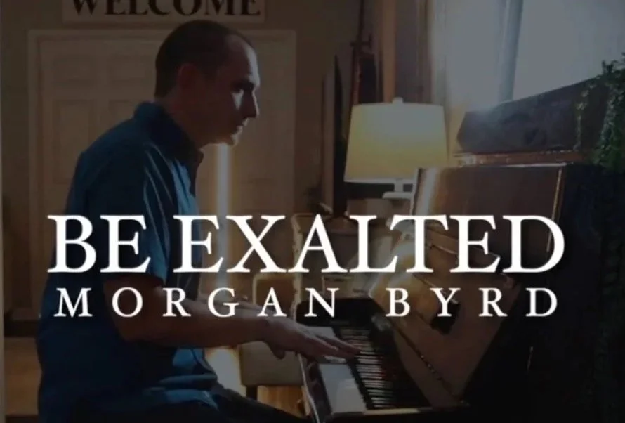 A man playing the piano in a cozy, warmly lit room with a lamp and a welcome sign in the background, with overlaid text that reads 'Be Exalted Morgan Byrd'.