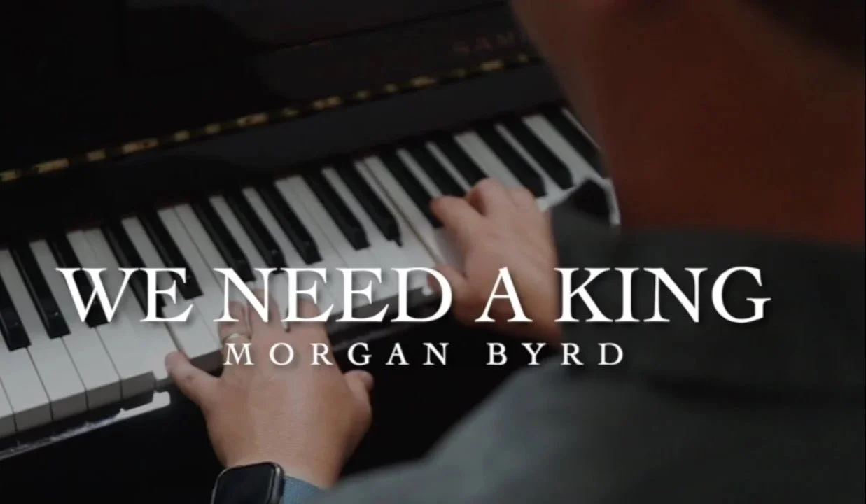 Close-up of a person's hands playing a piano, with the title 'We Need a King' and author 'Morgan Byrd' superimposed on the image.