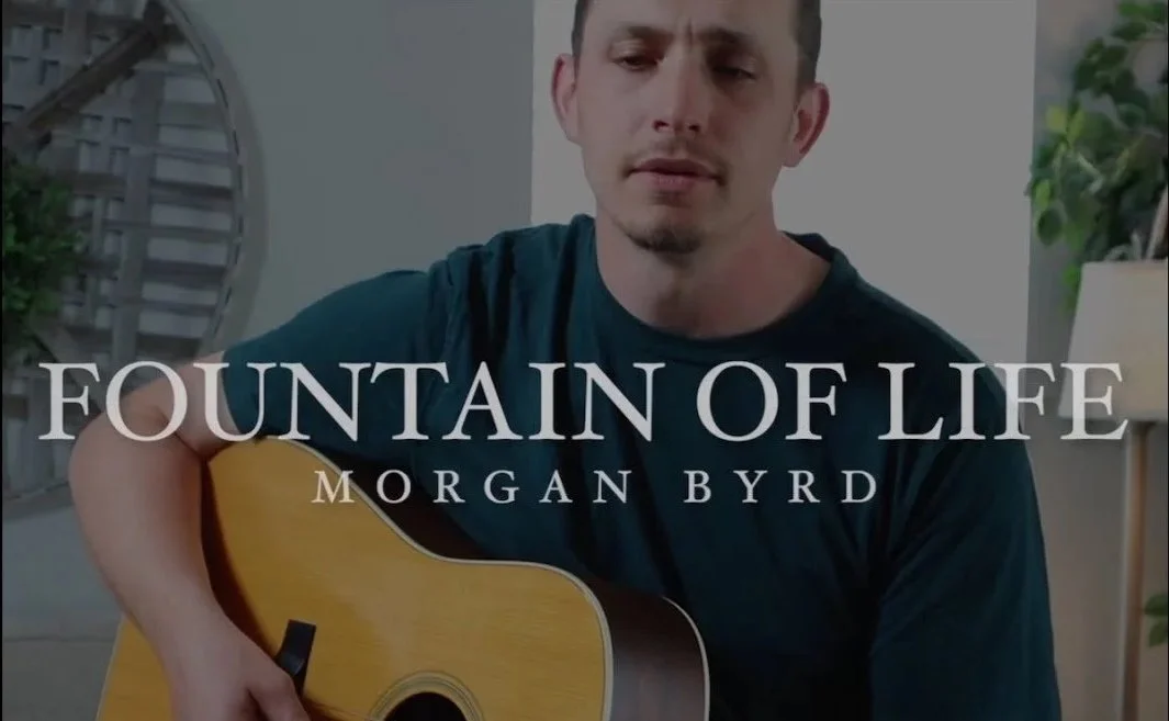 A man playing guitar indoors, with text overlaying that reads 'Fountain of Life Morgan Byrd'.