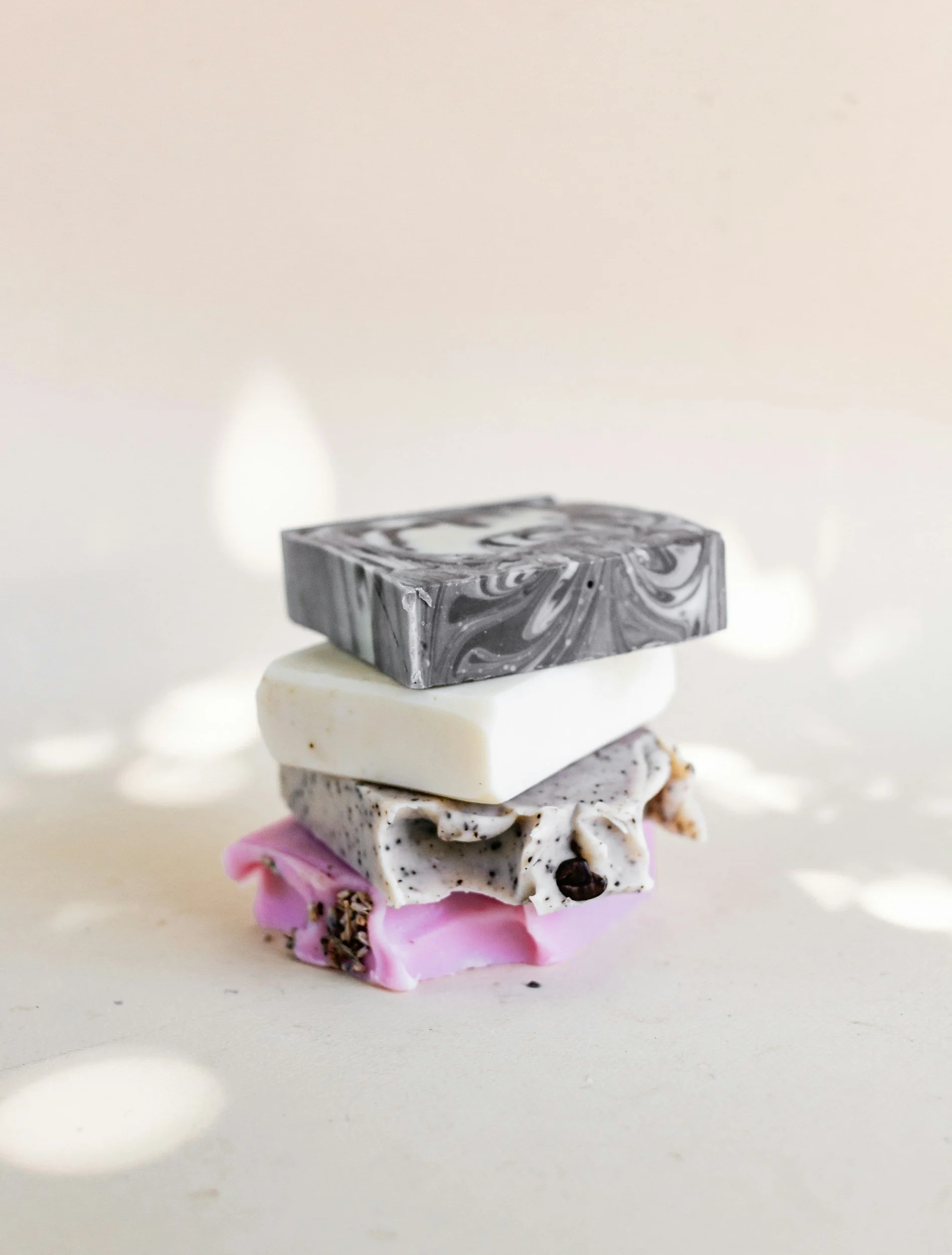 Stacked handmade soap bars in black and white swirls, white, speckled, and pink colors on a light background.