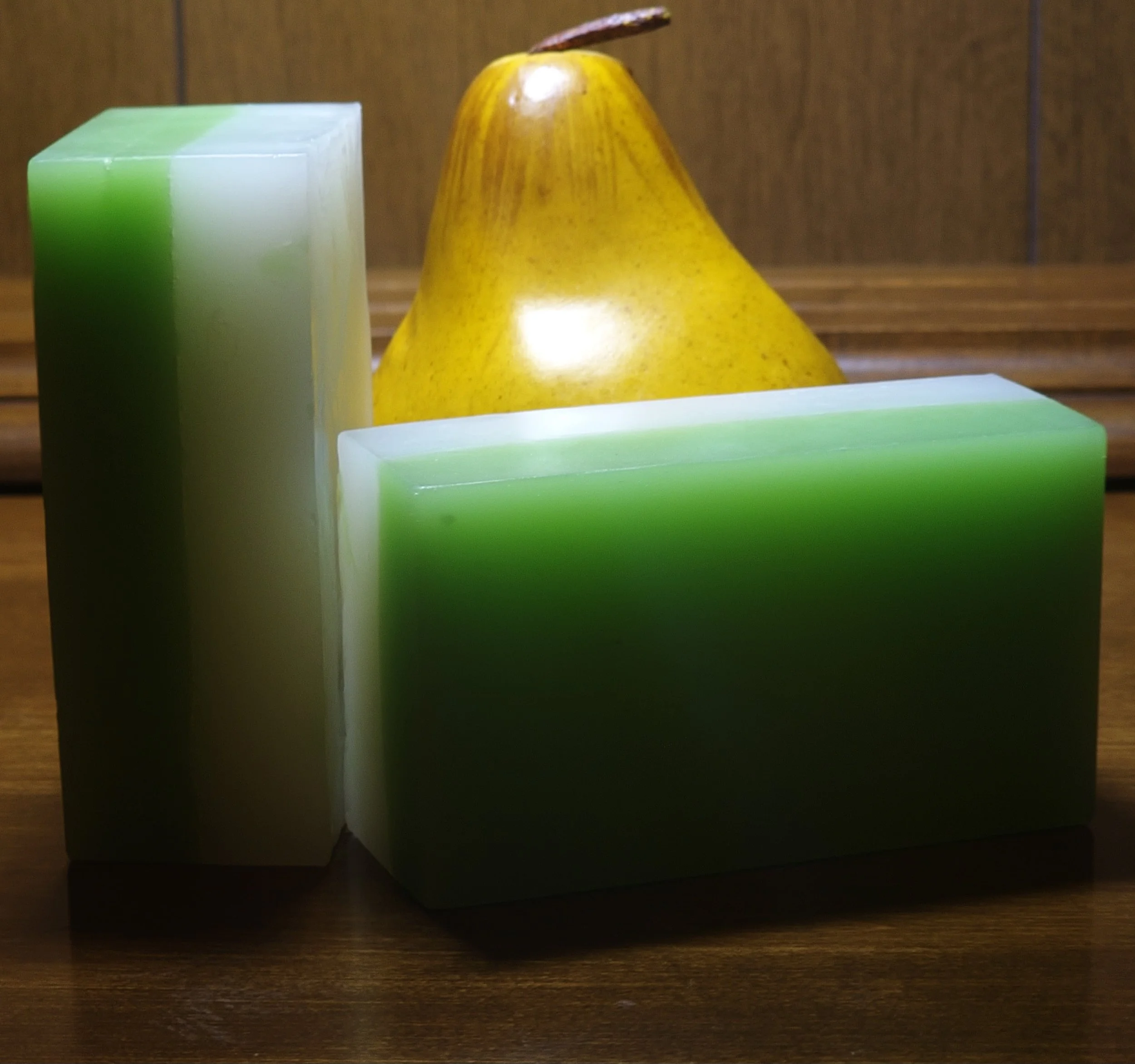 A yellow pear, two large soap bars with green and white gradient colors, and a wooden background.