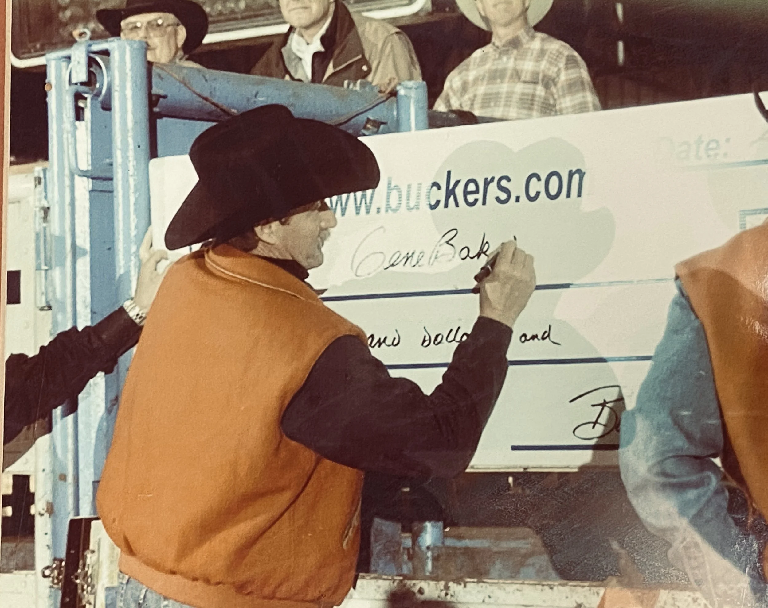 Man in cowboy hat signing a large check for Buckers.com, with other people watching