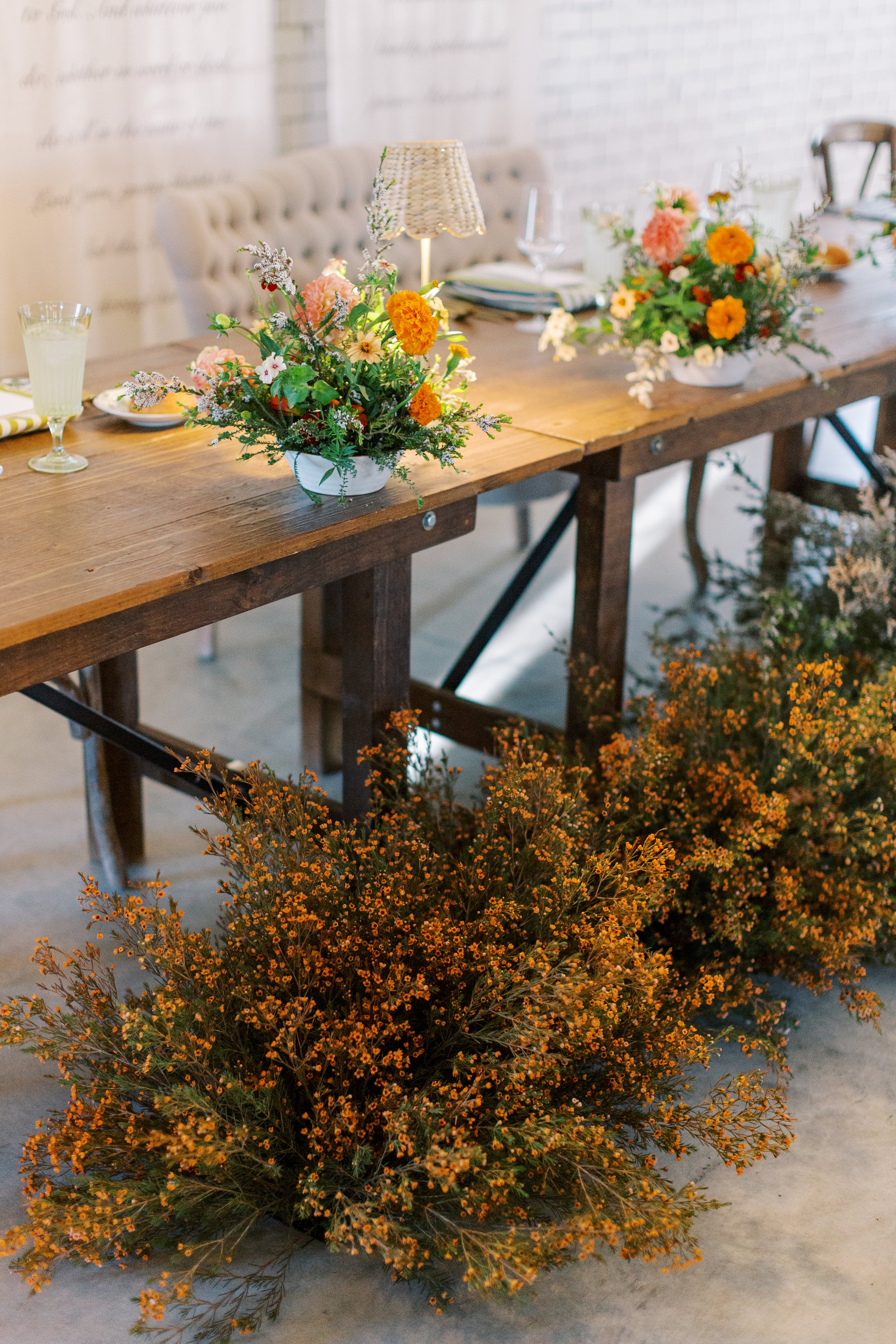 Rustic wooden table decorated with floral arrangements, surrounded by orange flowers on the floor.