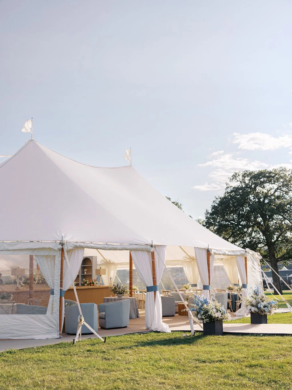 Event tent set up on a grassy lawn with white curtains and floral arrangements.