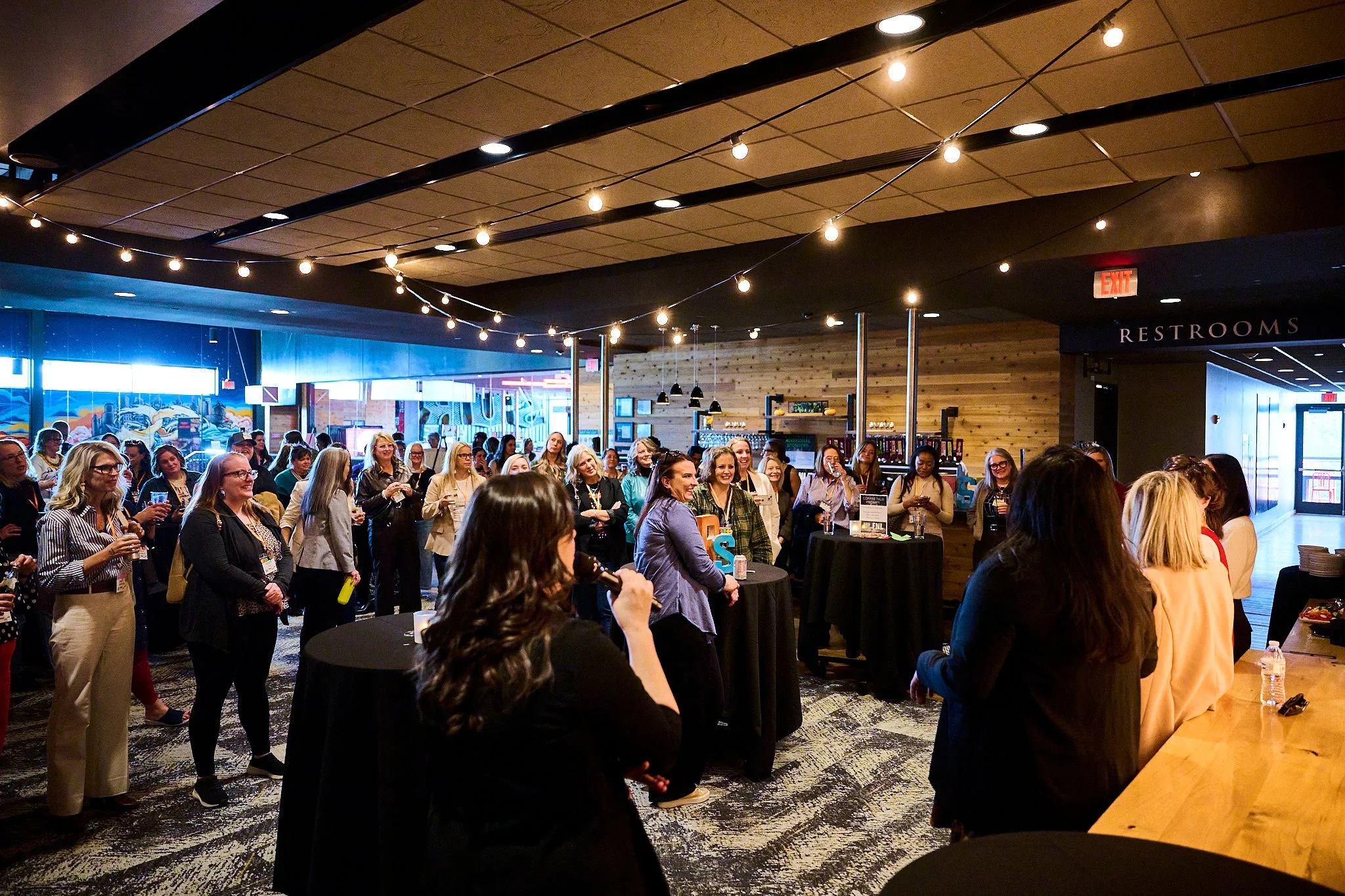 Group of women attending a social event in a modern indoor venue with string lights overhead.