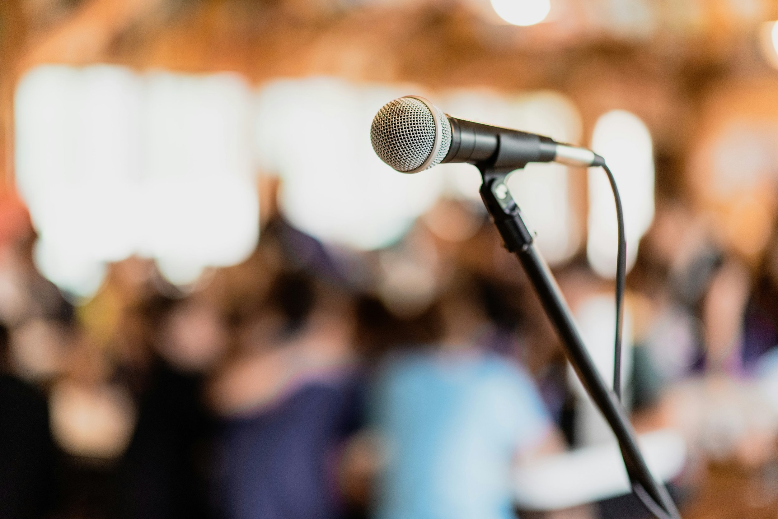 Close-up of a microphone on a stand in front of a blurred audience at a conference or event.