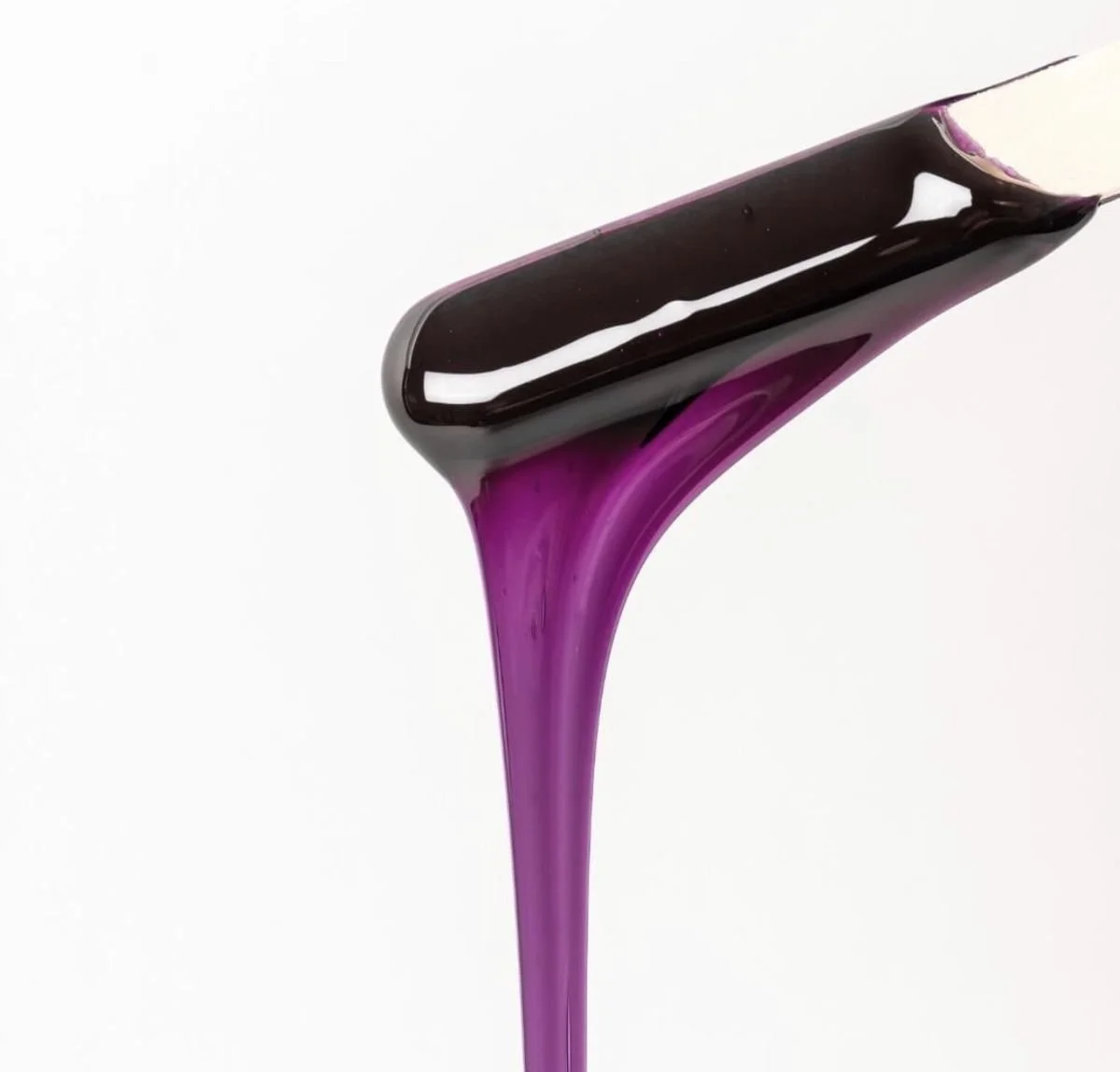 Close-up of a spoon with shiny black and purple liquid dripping off the edge