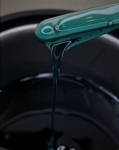 Greenish-blue liquid being poured into a black pan.
