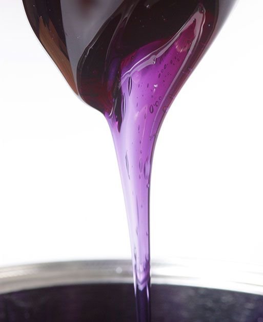 Purple liquid being poured from a dark bottle into a container.