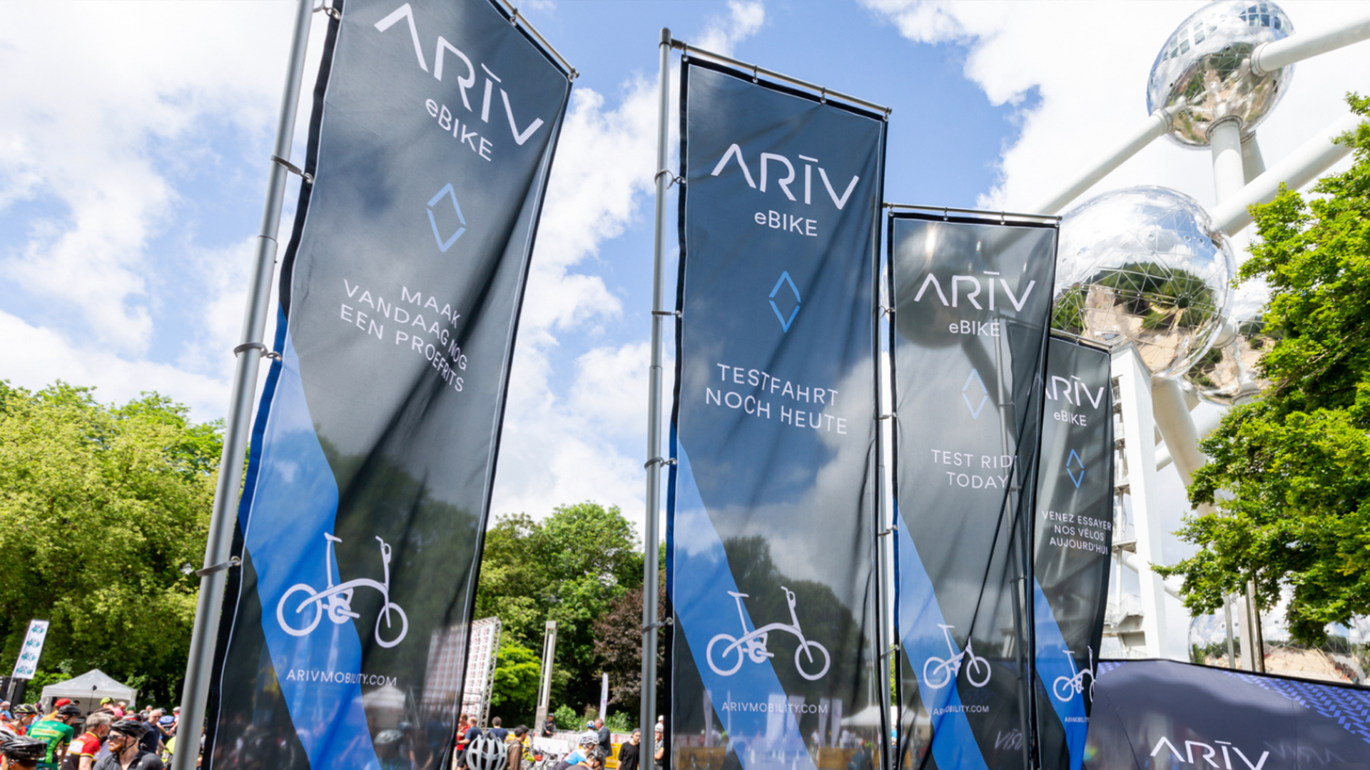 Multiple vertical banners advertising ARIV eBike, with messages in Dutch and English about test rides and promotions, set outdoors.