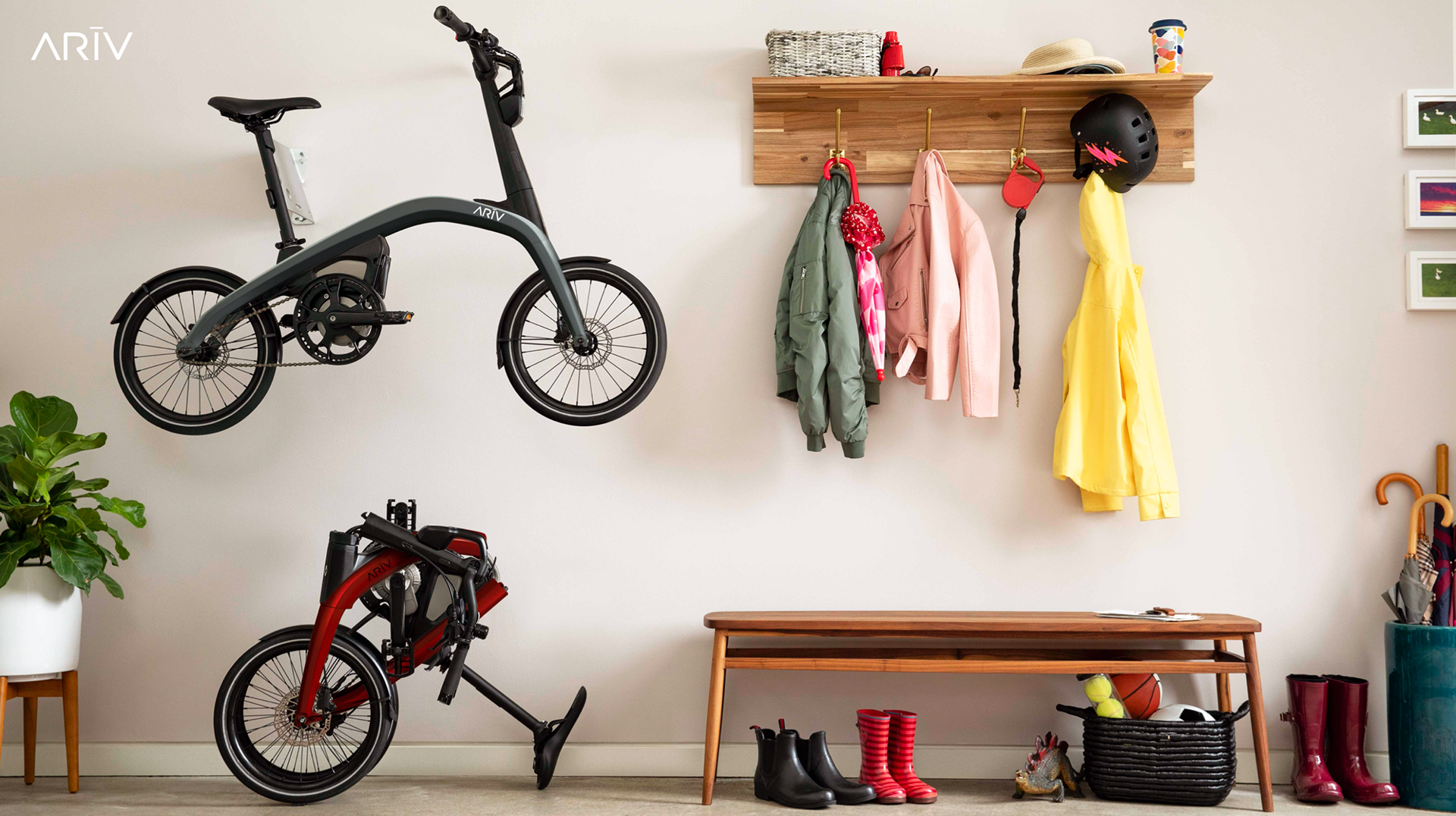 Indoor entryway with two e-bikes, a plant in a white pot, a wooden bench, waterproof boots, rain boots, and shoes, hooks with jackets, a helmet, a hat, gloves, and a water bottle, and magnetic picture frames on a white wall.