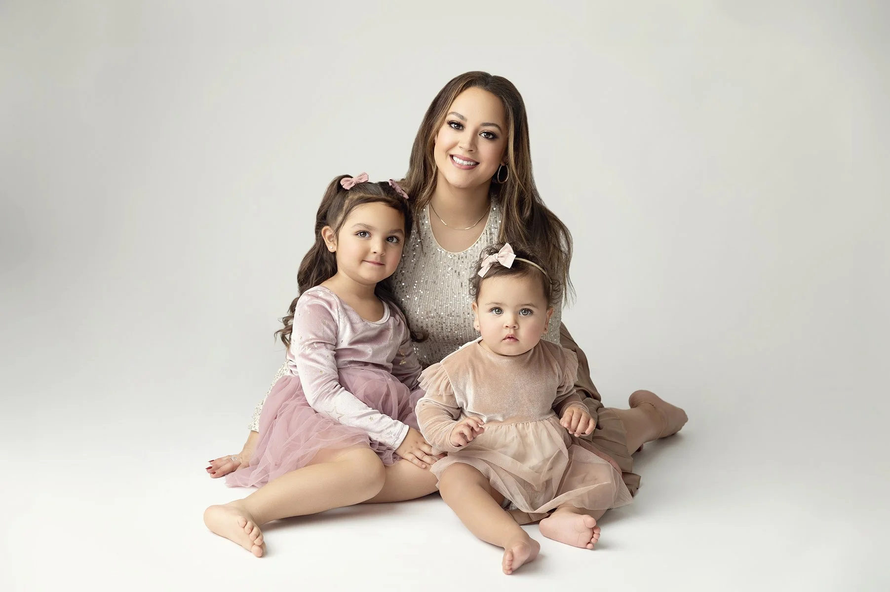 A woman with two young girls sitting on a white background.