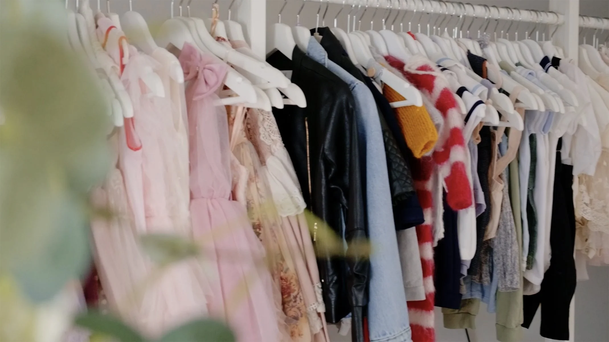 Clothing rack with various children's dresses, shirts, and jackets on white hangers in a store.