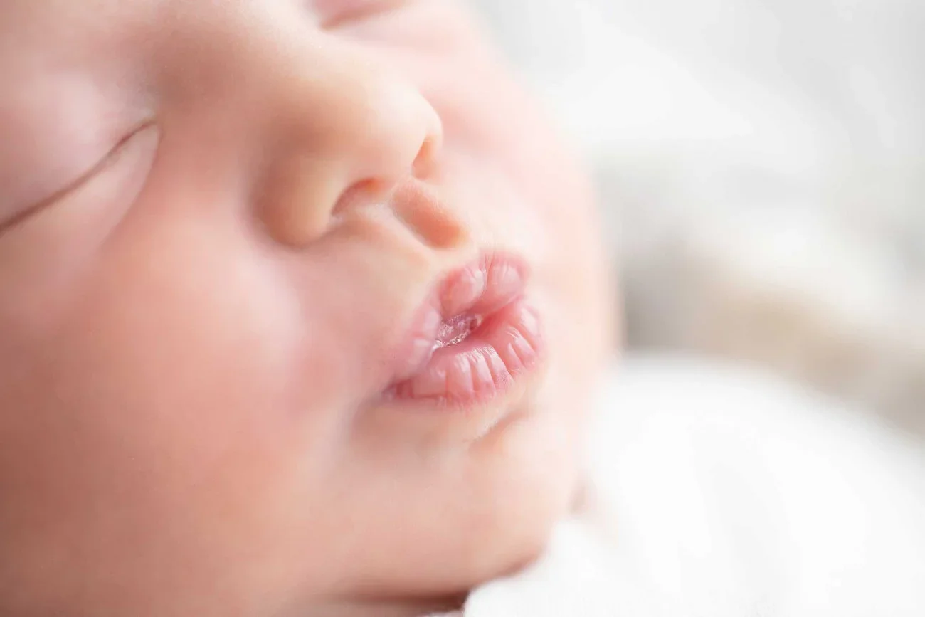Close-up of a newborn baby's face with closed eyes and lips slightly pursed.