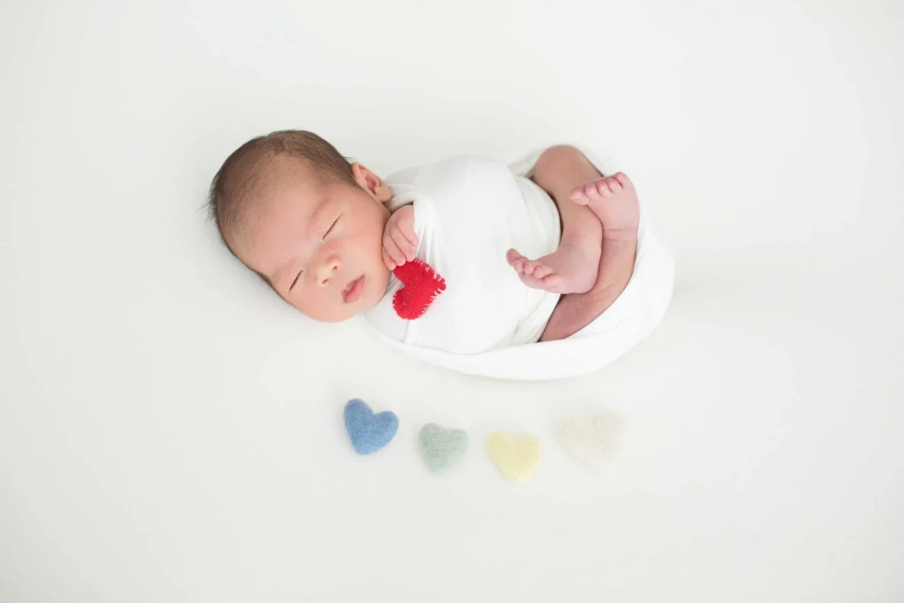 Neonatal baby sleeping on white surface with fuzzy colorful heart shapes underneath