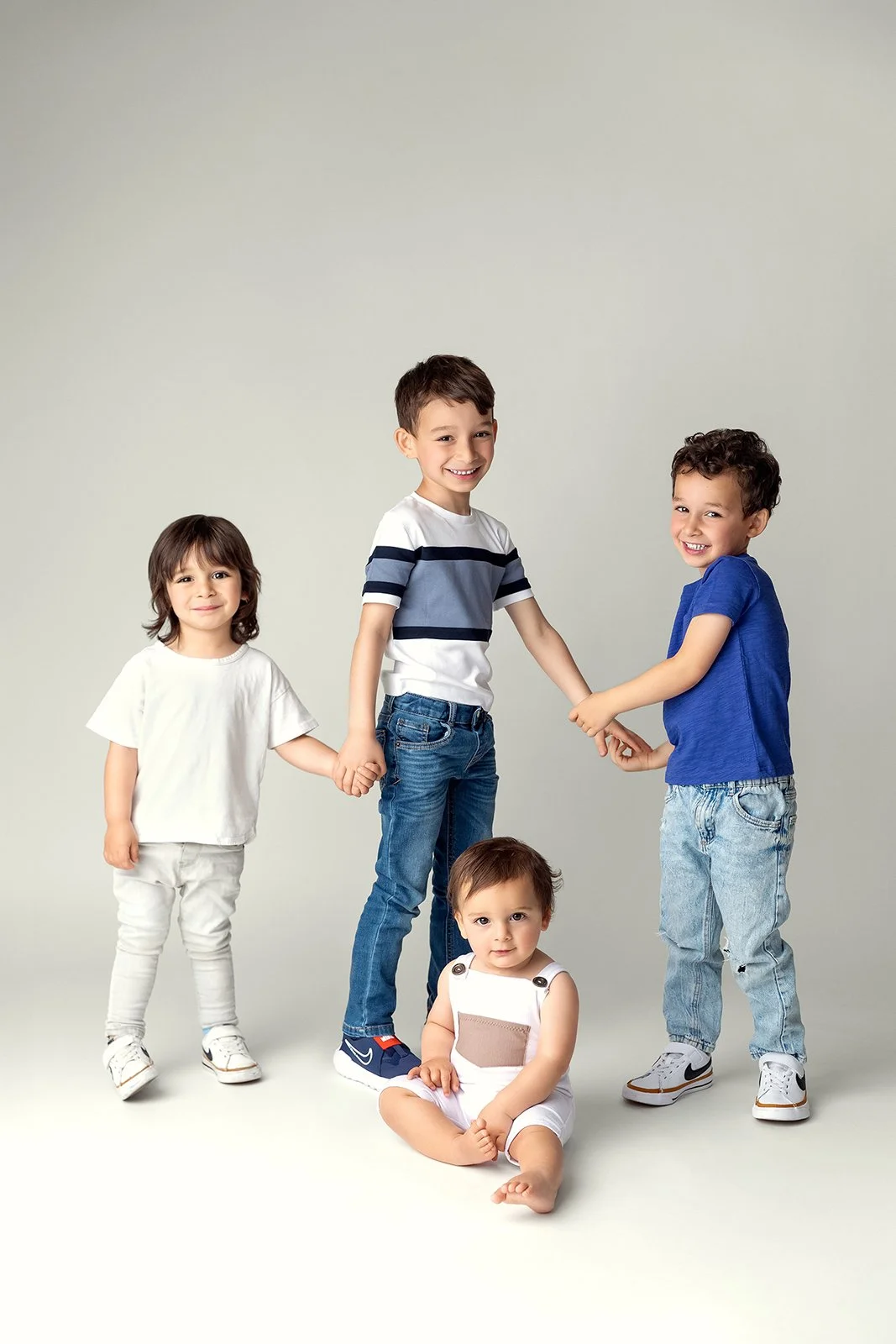 Four children standing and holding hands in a studio against a plain background, smiling.