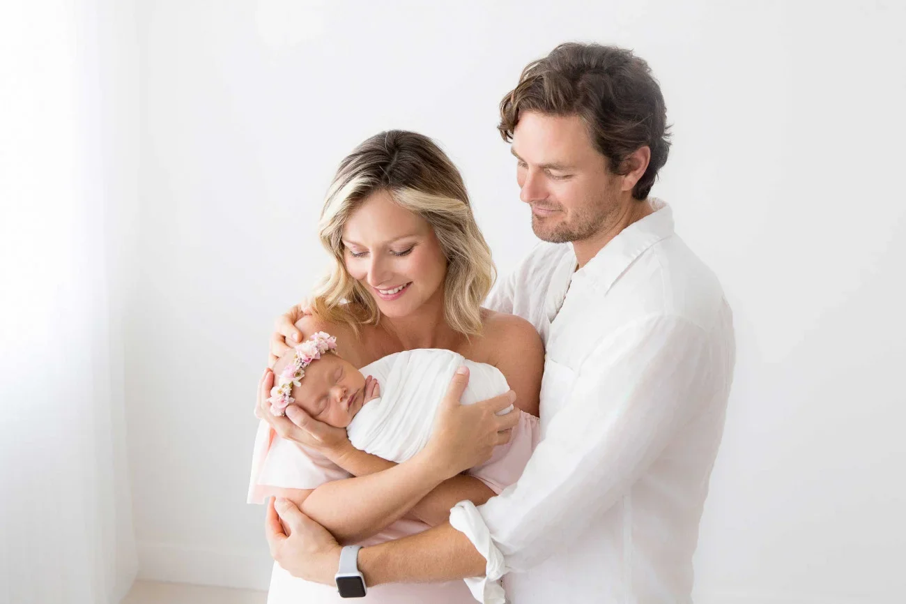 Happy family with a mother, father, and newborn baby in a bright room.