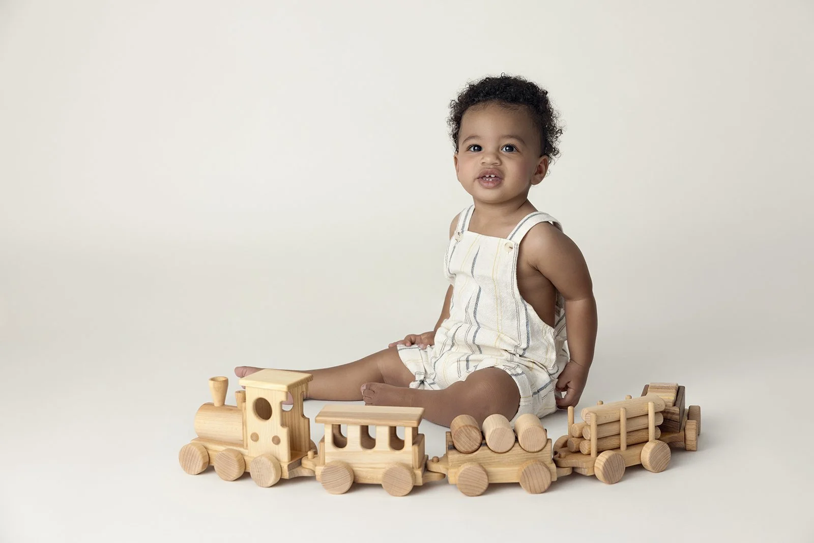 Young child sitting on the floor surrounded by wooden toy train