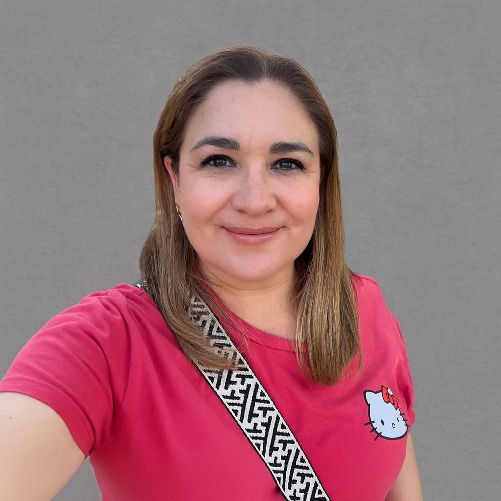 Retrato de una mujer sonriendo con camiseta rosa y el logo de Hello Kitty, frente a una pared gris.
