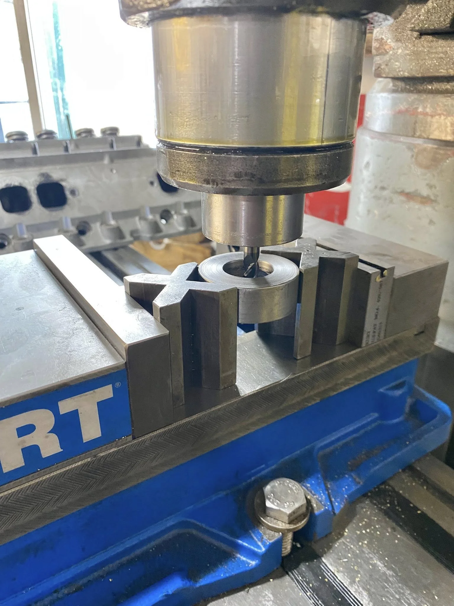 A drill press drilling into a metal piece held in a vice.