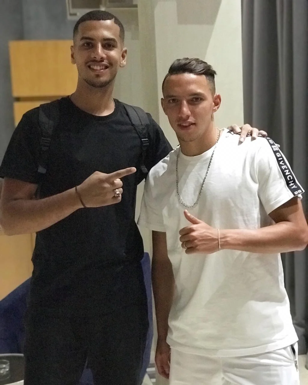 Deux jeunes hommes souriants posent ensemble; l'un porte un t-shirt noir, l'autre un t-shirt blanc avec des bandes Givenchy, et fait un geste de pouce levé. Best barber shop salon de coiffure Marrakech
