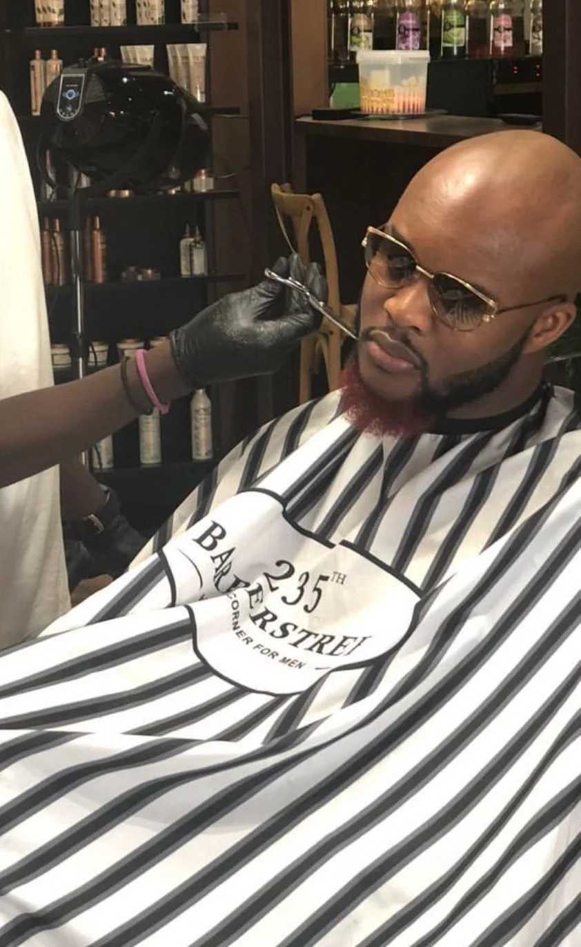 Un homme chauve avec une barbe rouge, portant des lunettes de soleil, assis en salon de coiffure, prêt à recevoir une injection sous-cutanée. Best barber shop salon de coiffure Marrakech