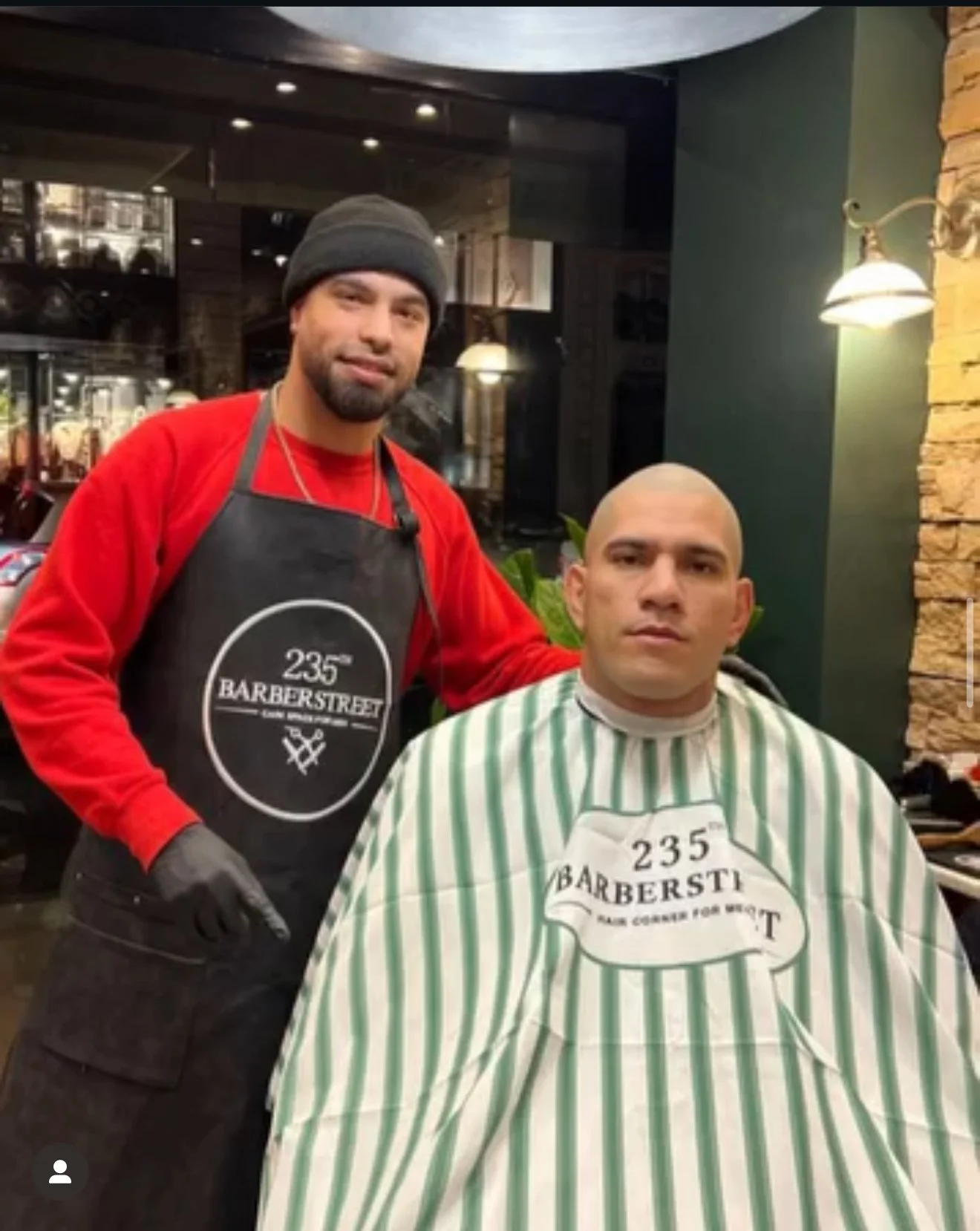 Un coiffeur masqué et un homme sous la cape de coupe. L'homme est déterminé. Le coiffeur porte un tablier noir avec le texte '235° BARBERSTREET' et un bonnet gris, l'autre homme porte une cape rayée verte et blanche. Best barber shop salon de coiffure