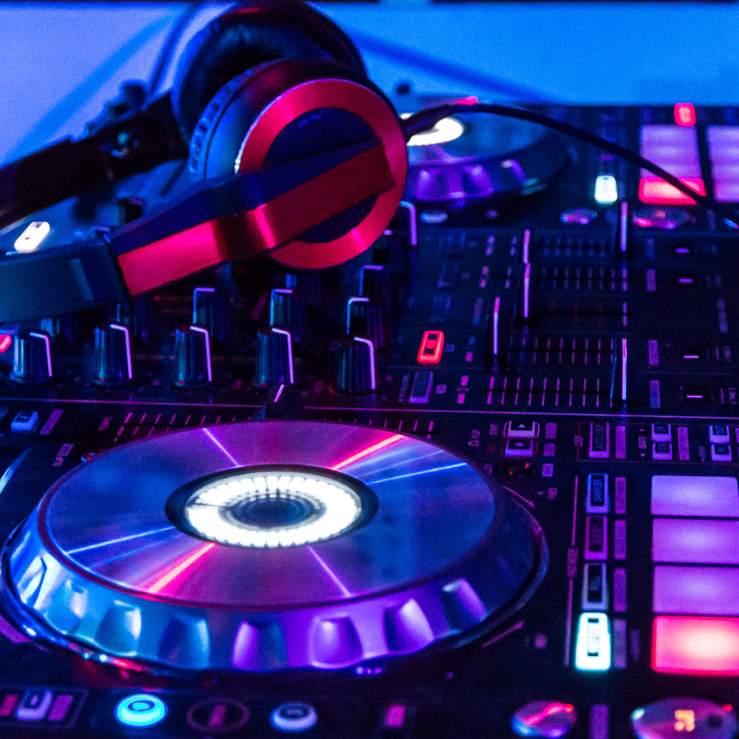 Close-up view of a DJ's turntable and mixer with glowing lights in purple, blue, and pink colors.