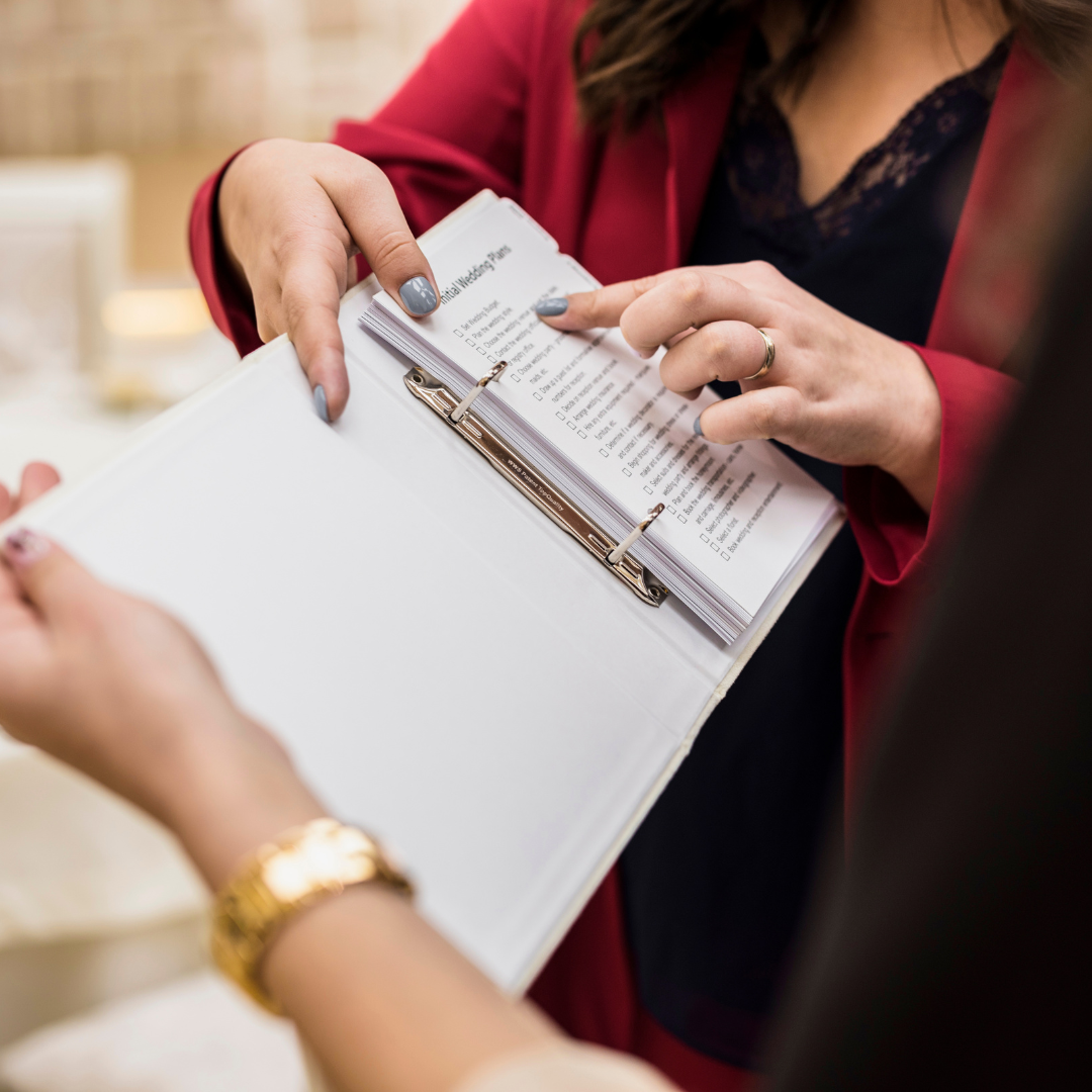 Person holding a binder with a checklist inside, pointing at the checklist, with another person nearby.