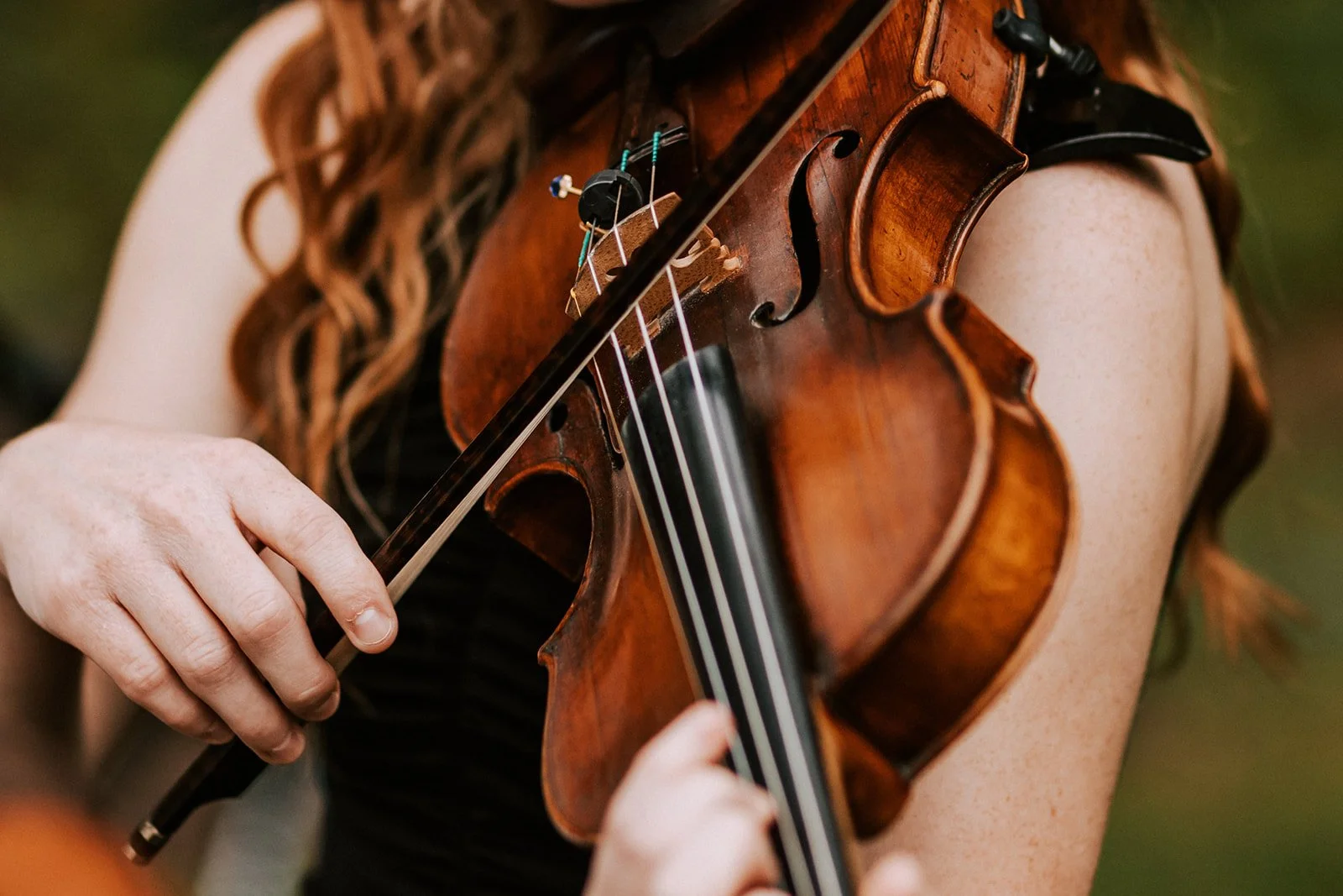 A person playing a violin outdoors, focusing on their hands and the violin.