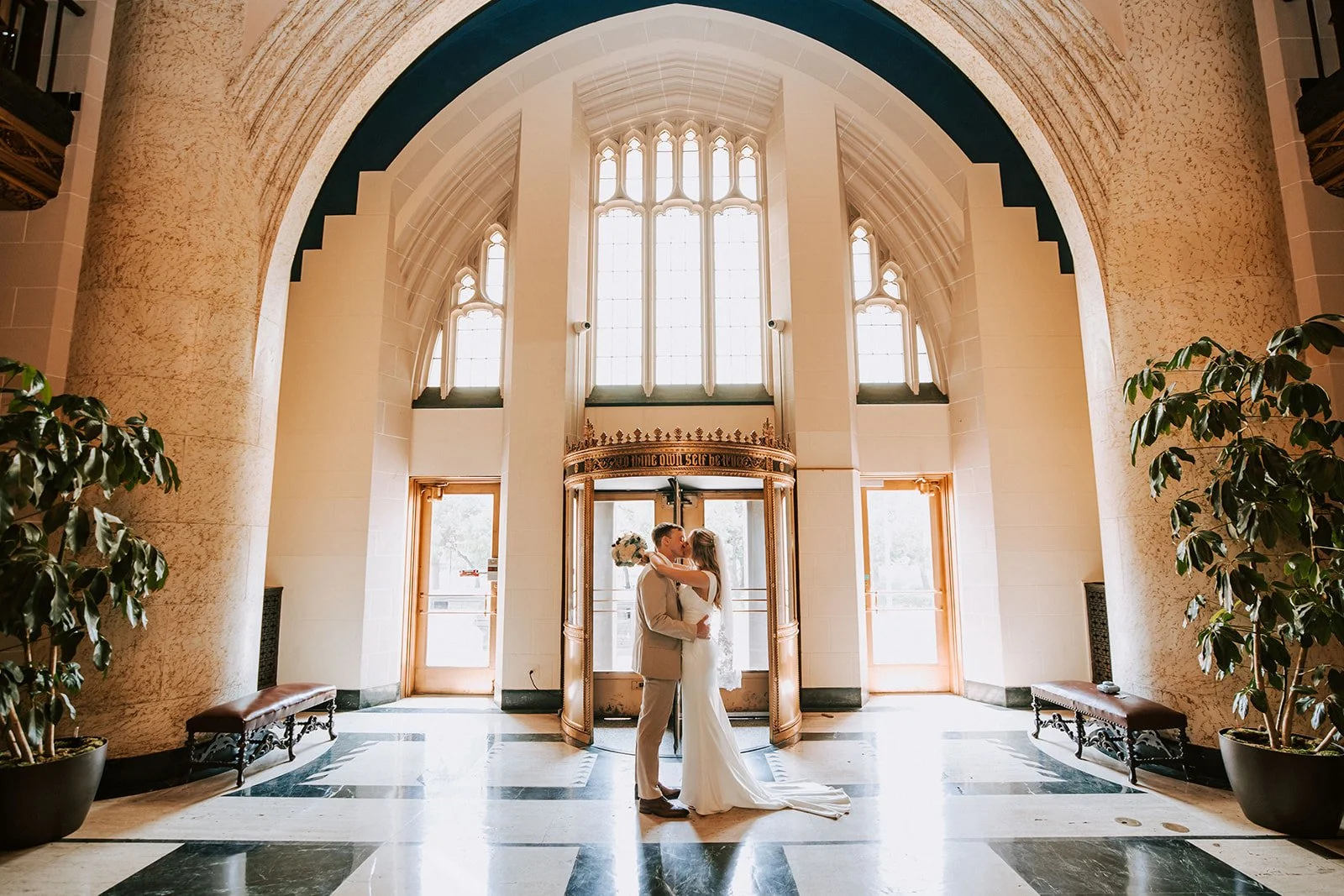 A bride and groom sharing a kiss inside a grand, cathedral-like church with high arched windows and gothic architecture.