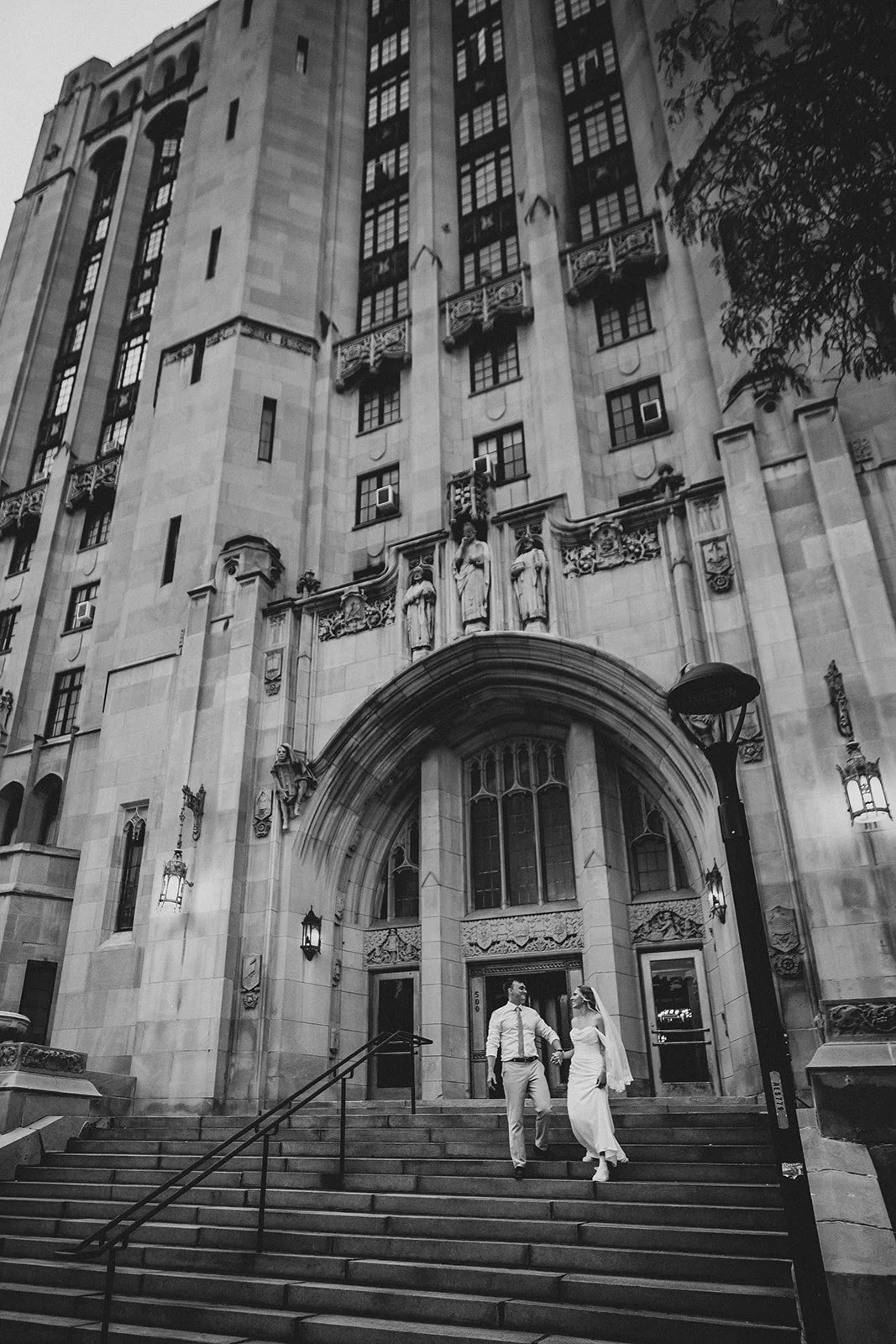 A black and white photo of an ornate historic building with statues and decorative carvings, showing a couple descending stairs.