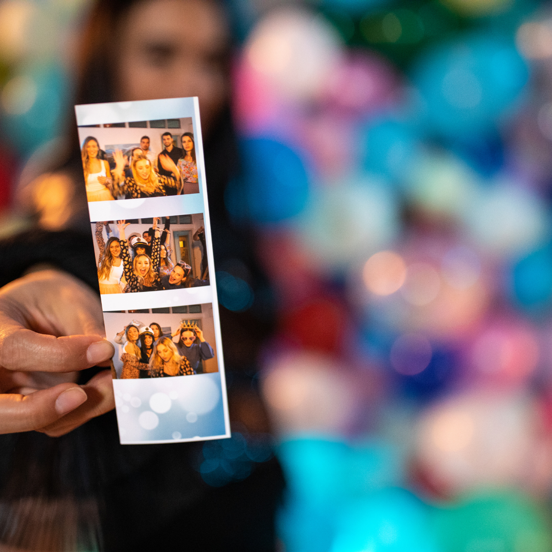 Person holding a photo strip with three images of friends celebrating and having fun at a party or event.