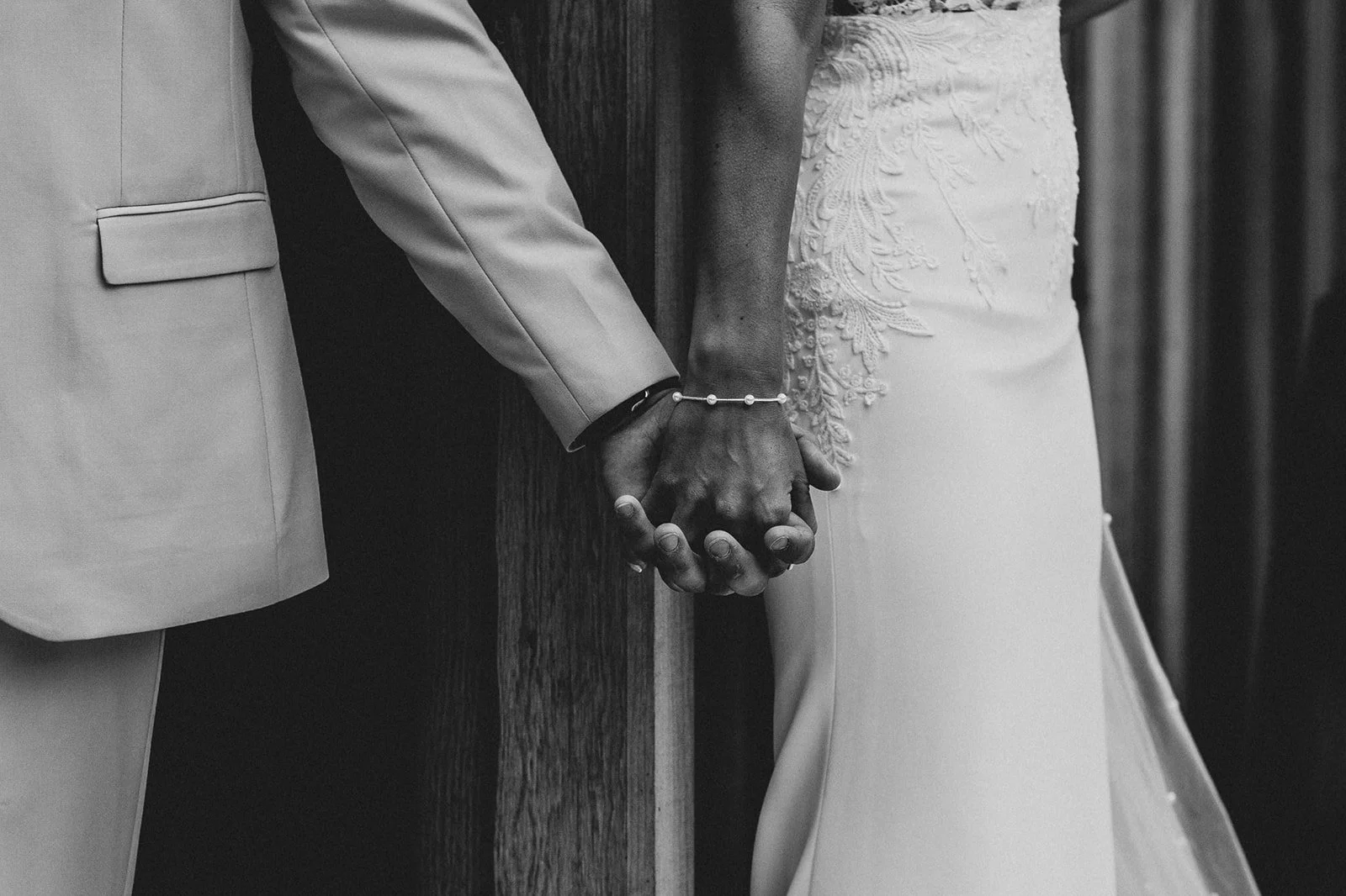 Close-up of a bride and groom holding hands during a wedding ceremony, with the bride in a lace wedding dress and the groom in a suit.